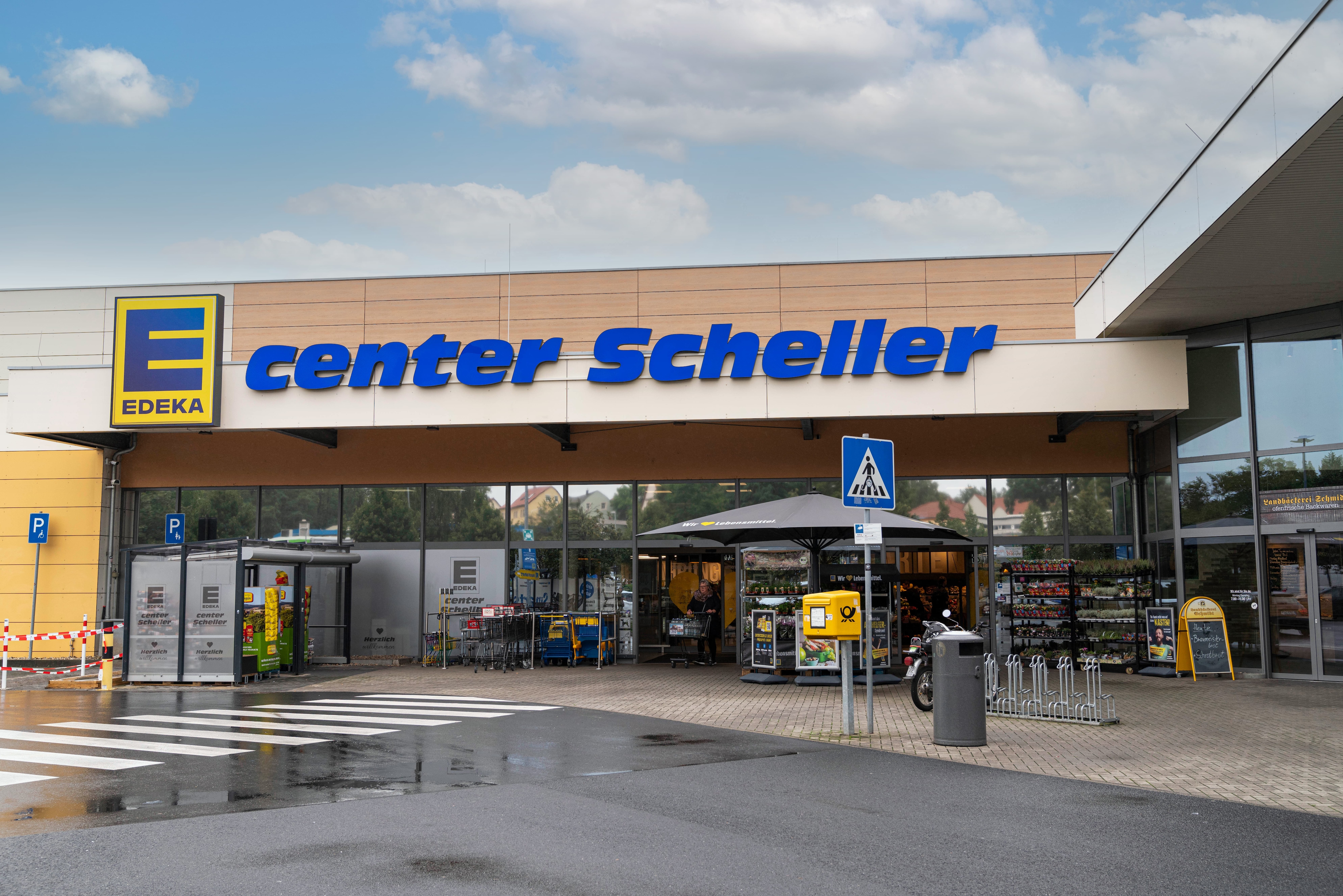 Der helle Eingang des EDEKA center Scheller vom verregneten Parkplatz aus gesehen.