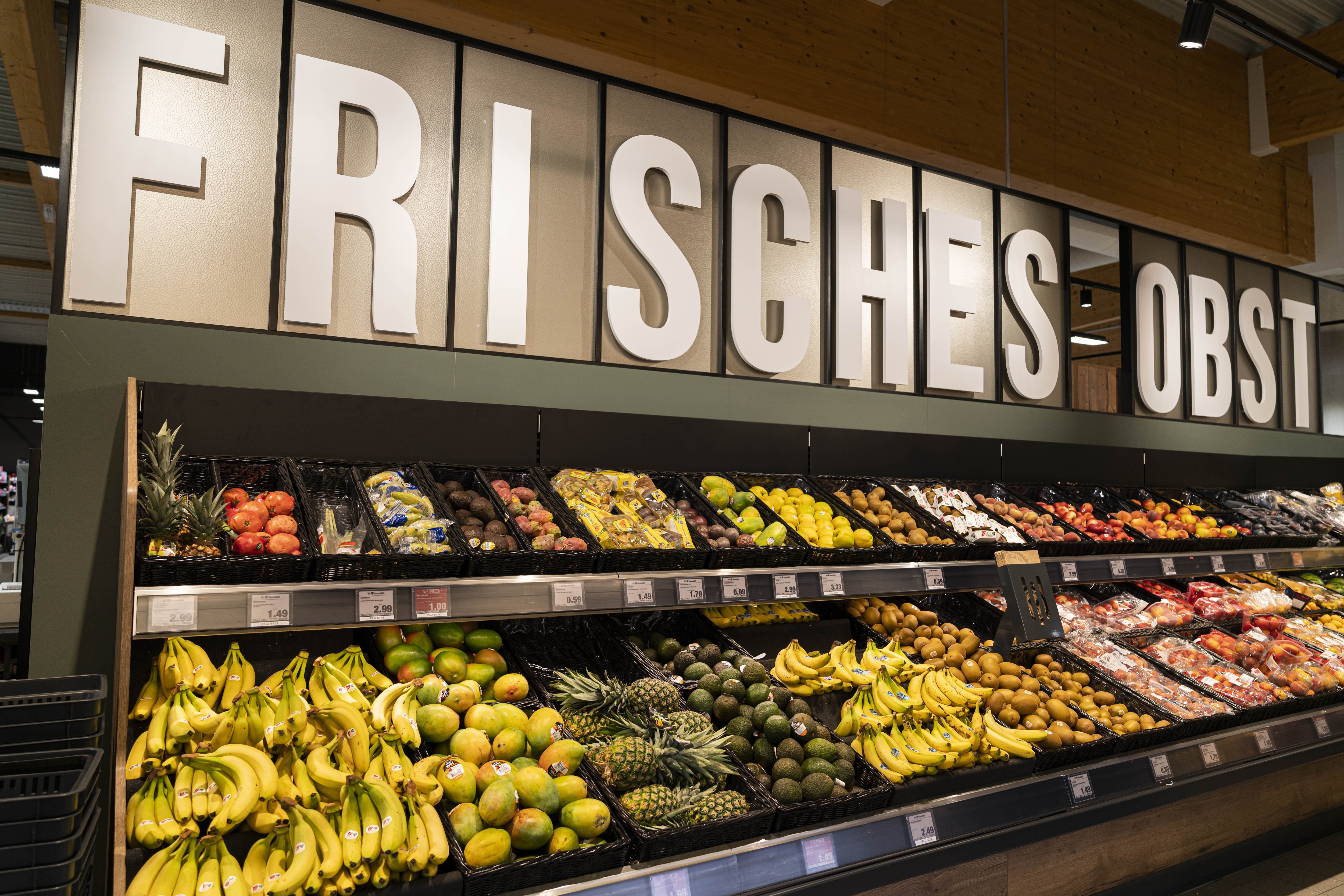 Über dem Obstregal mit Bananen und Zitrusfrüchten steht Frisches Obst.