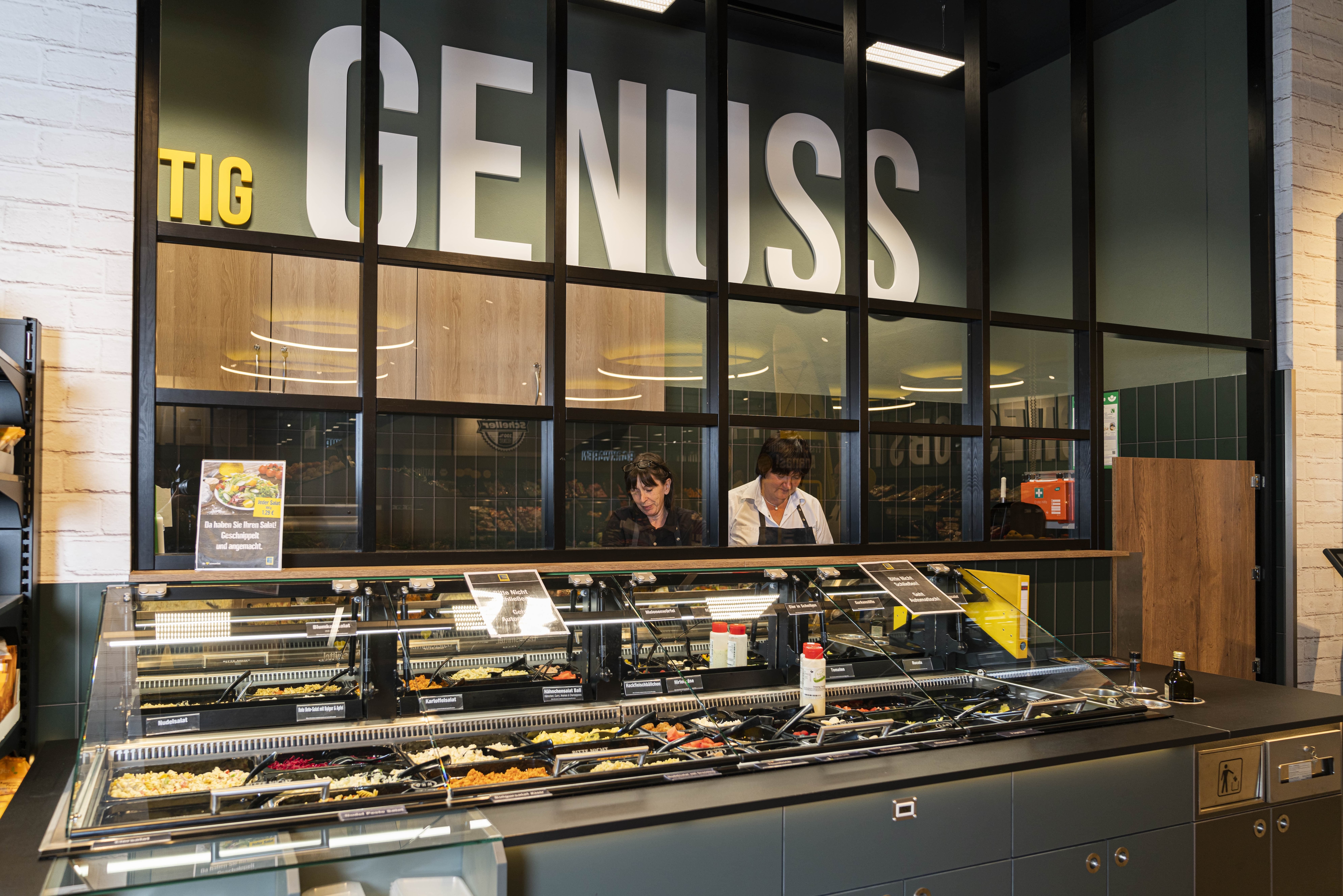 Hinter dem Tresen der Salatbar stehen zwei Frauen in EDEKA-Kleidung.