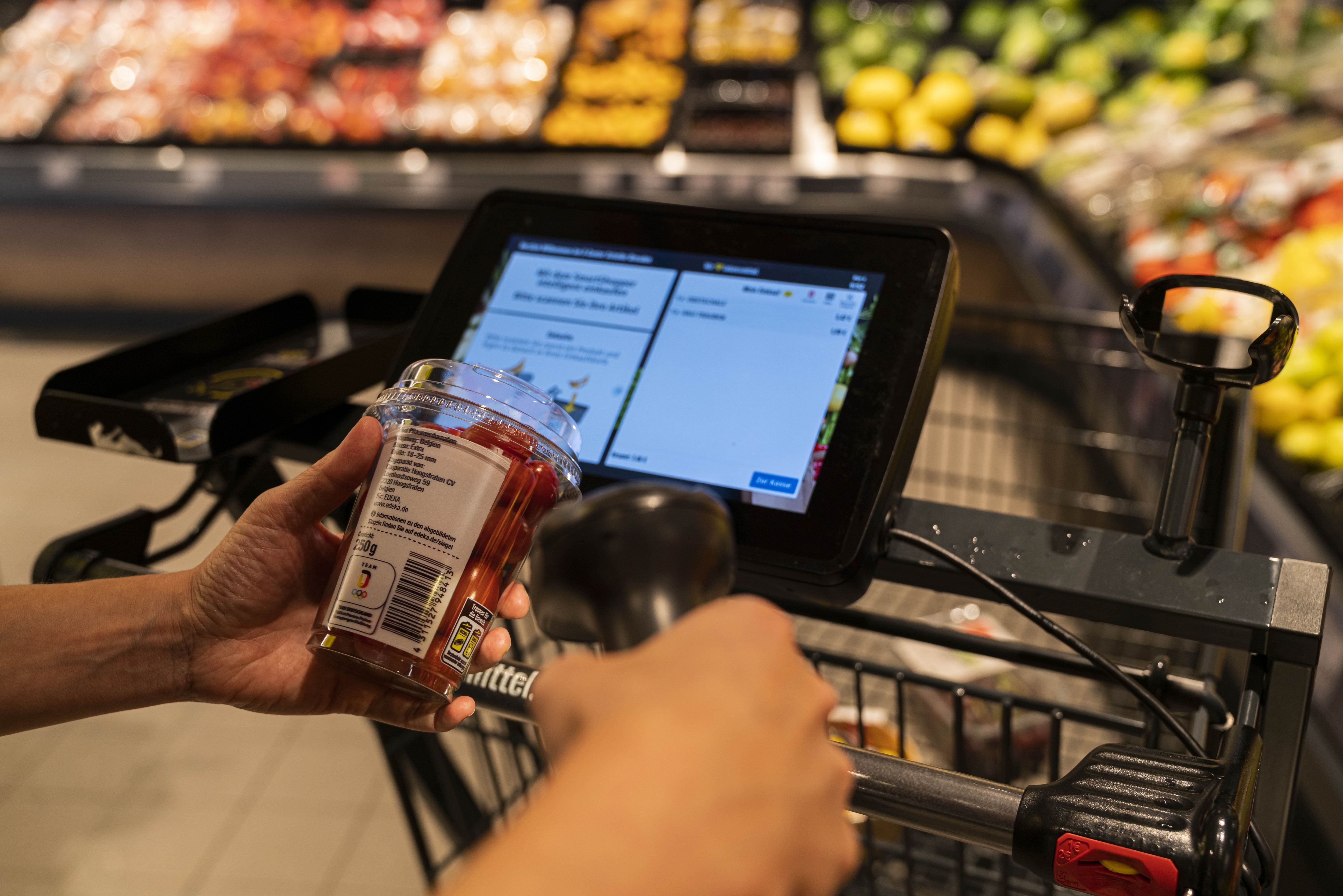 Eine Person scannt eine Packung Tomaten über dem Display an seinem Einkaufswagen.