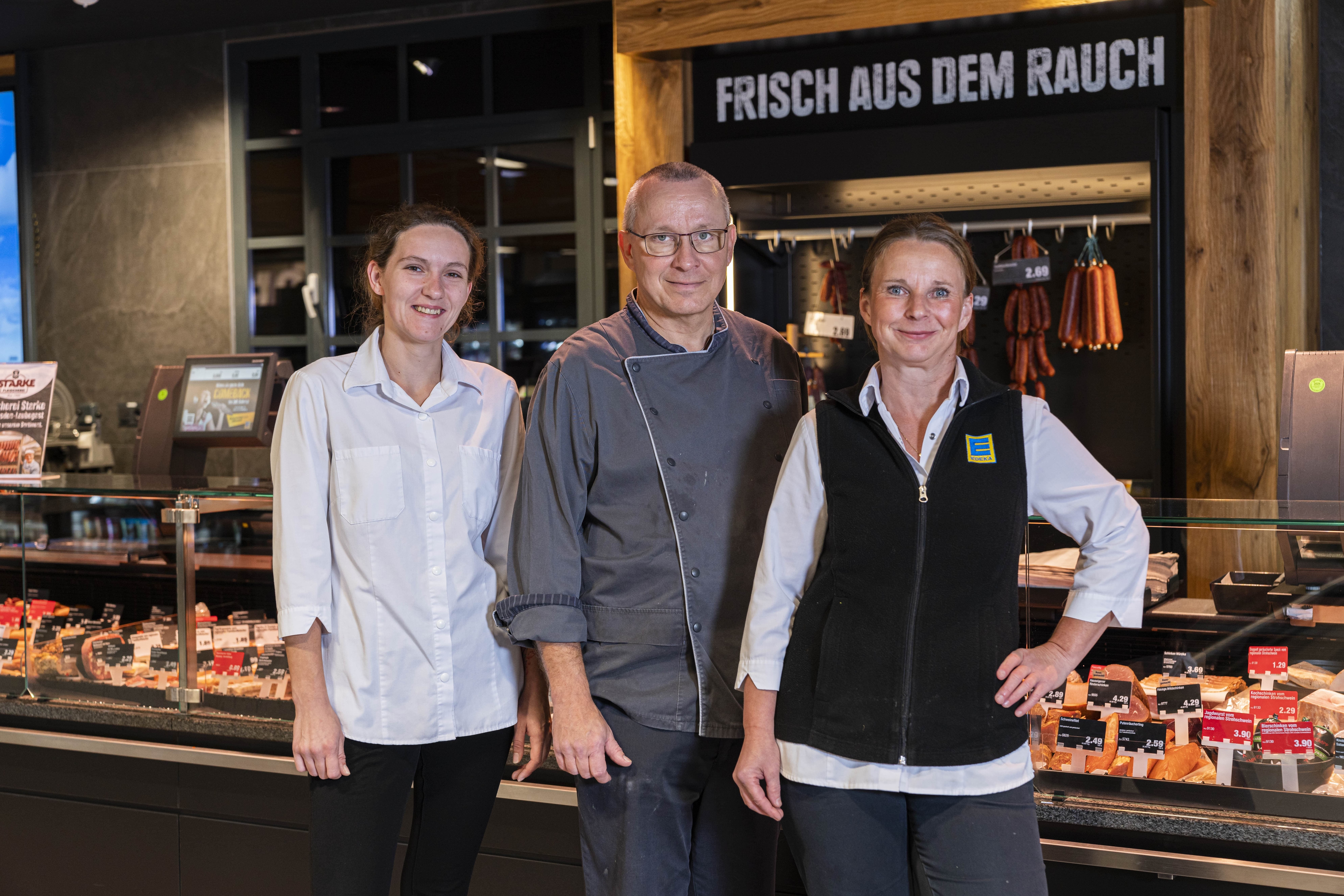 Zwei Frauen und ein Mann in Edeka-Kleidung stehen vor der Frischetheke.