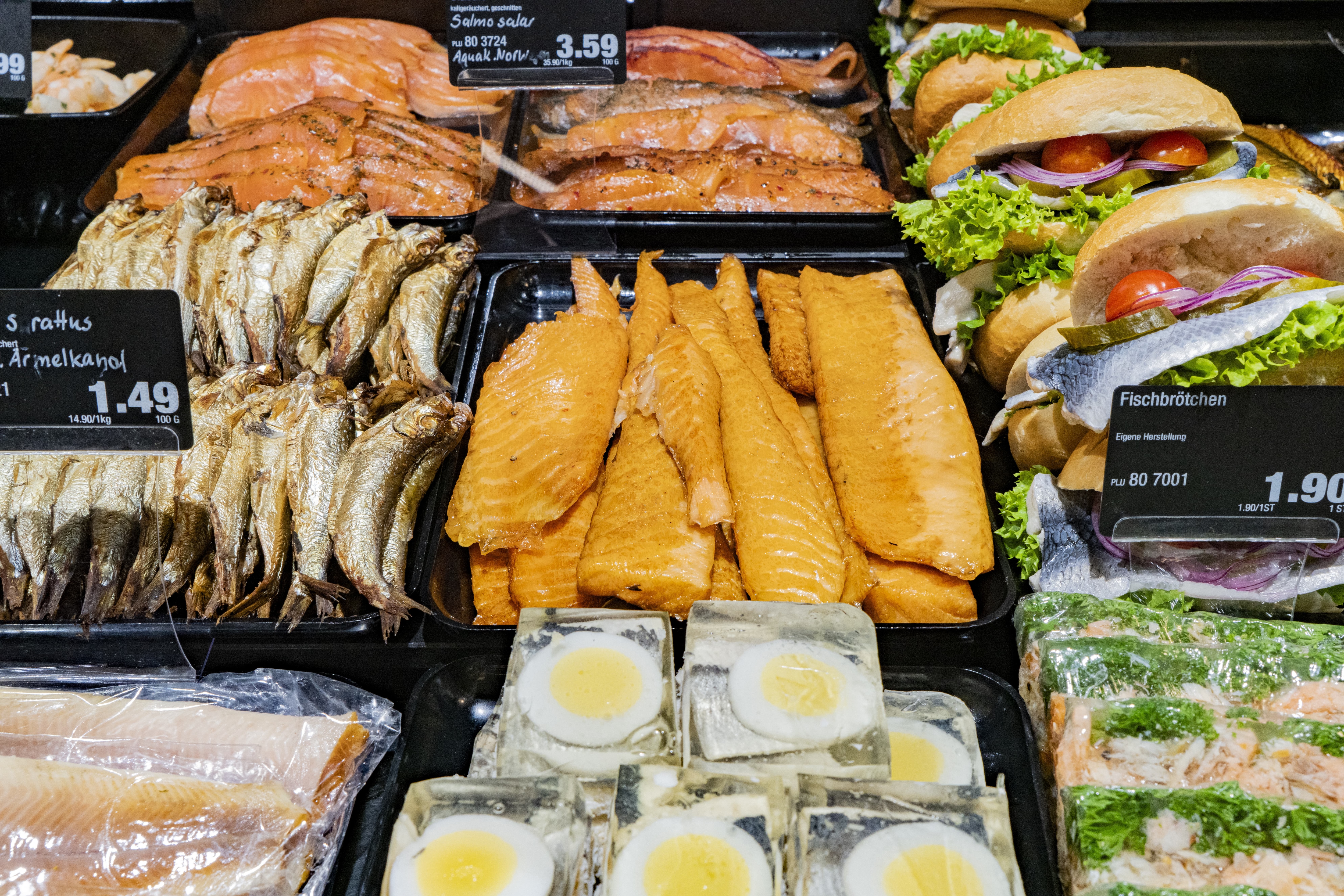 Räucherfisch und Fischbrötchen in einer Auslage mit Preisschildern.