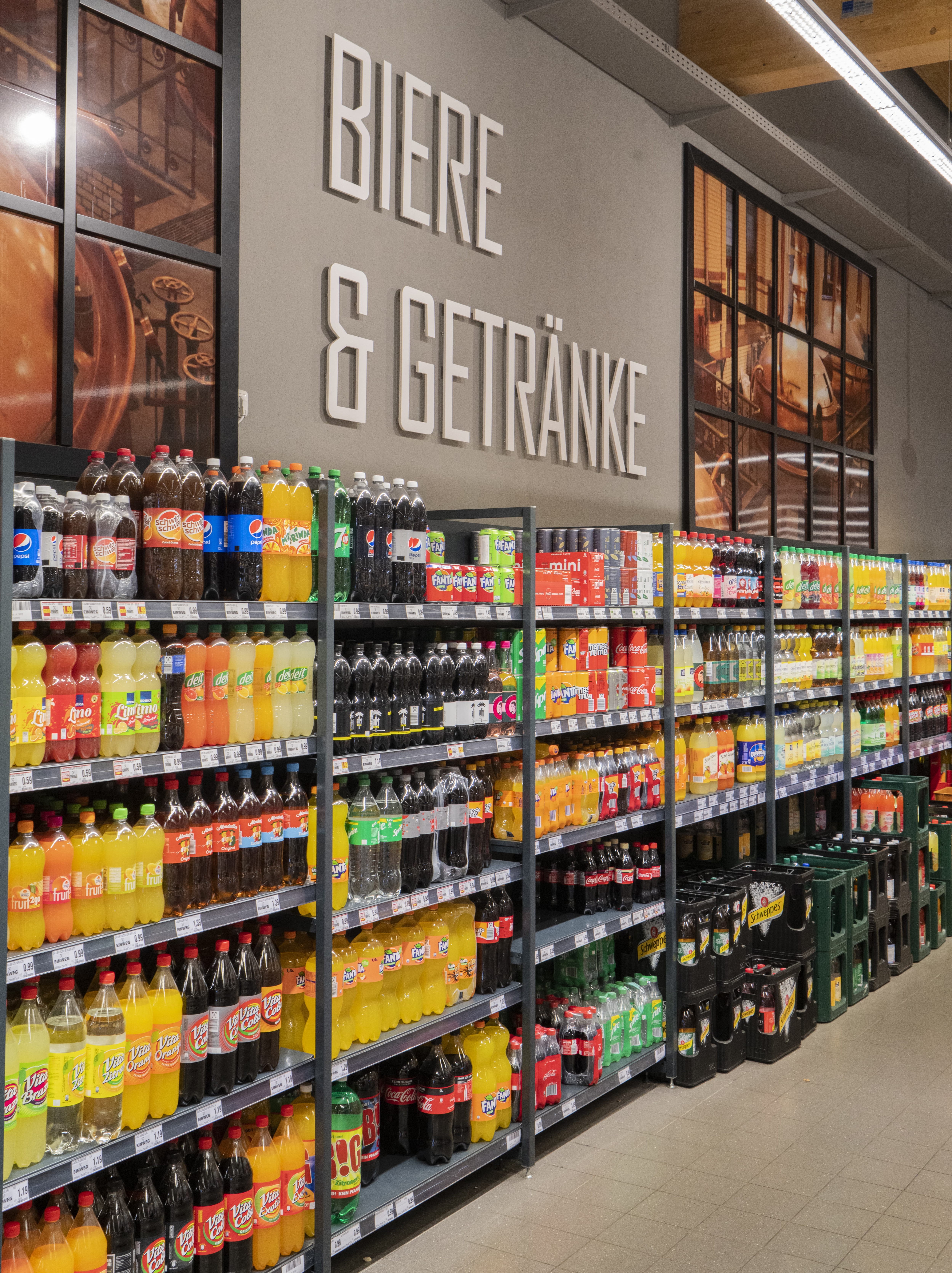Über dem Regal mit Limonaden steht Bier und Getränke an der Wand.