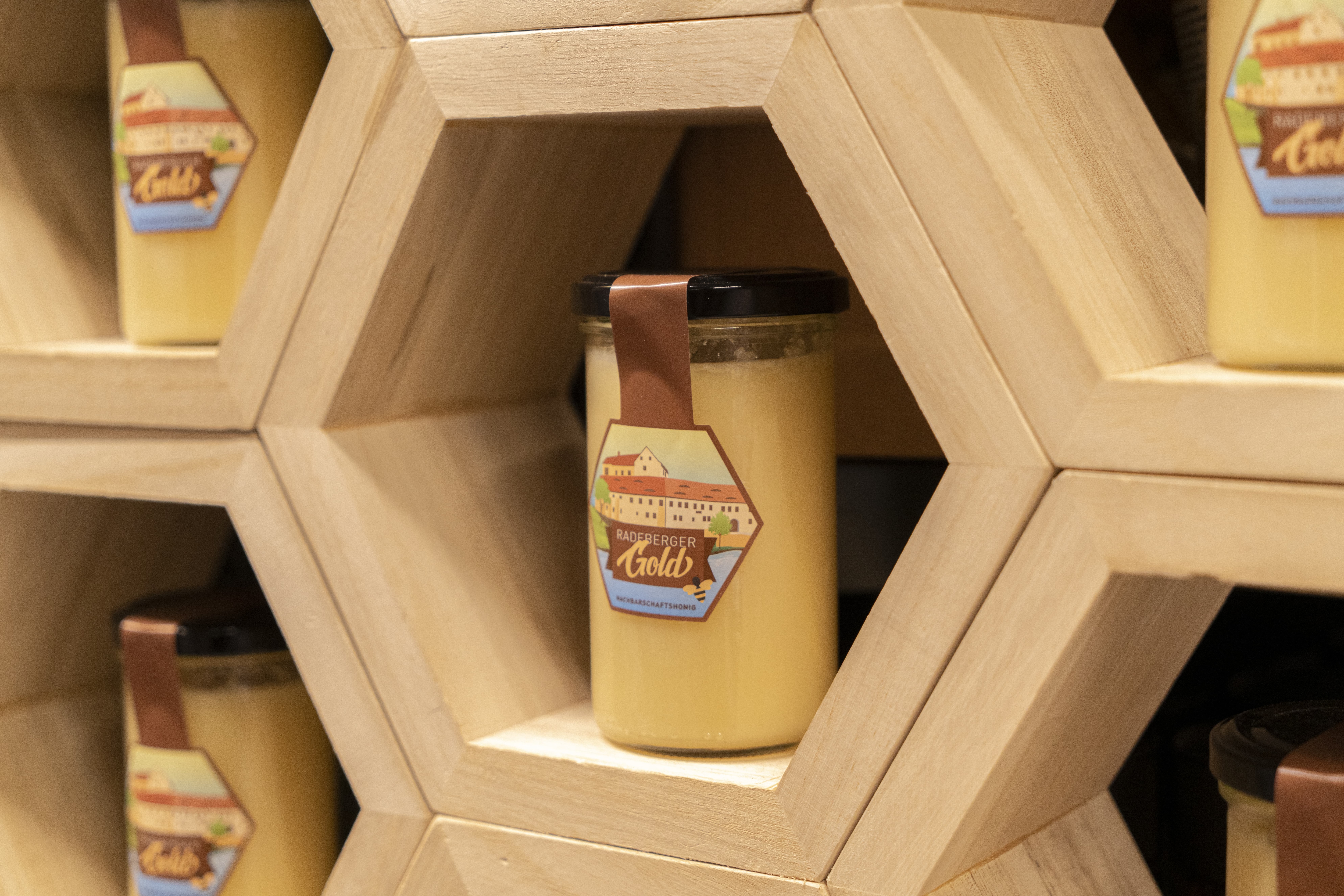 In einer Wabe aus Holz steht ein Glas Honig mit dem Label Radeberger Gold.
