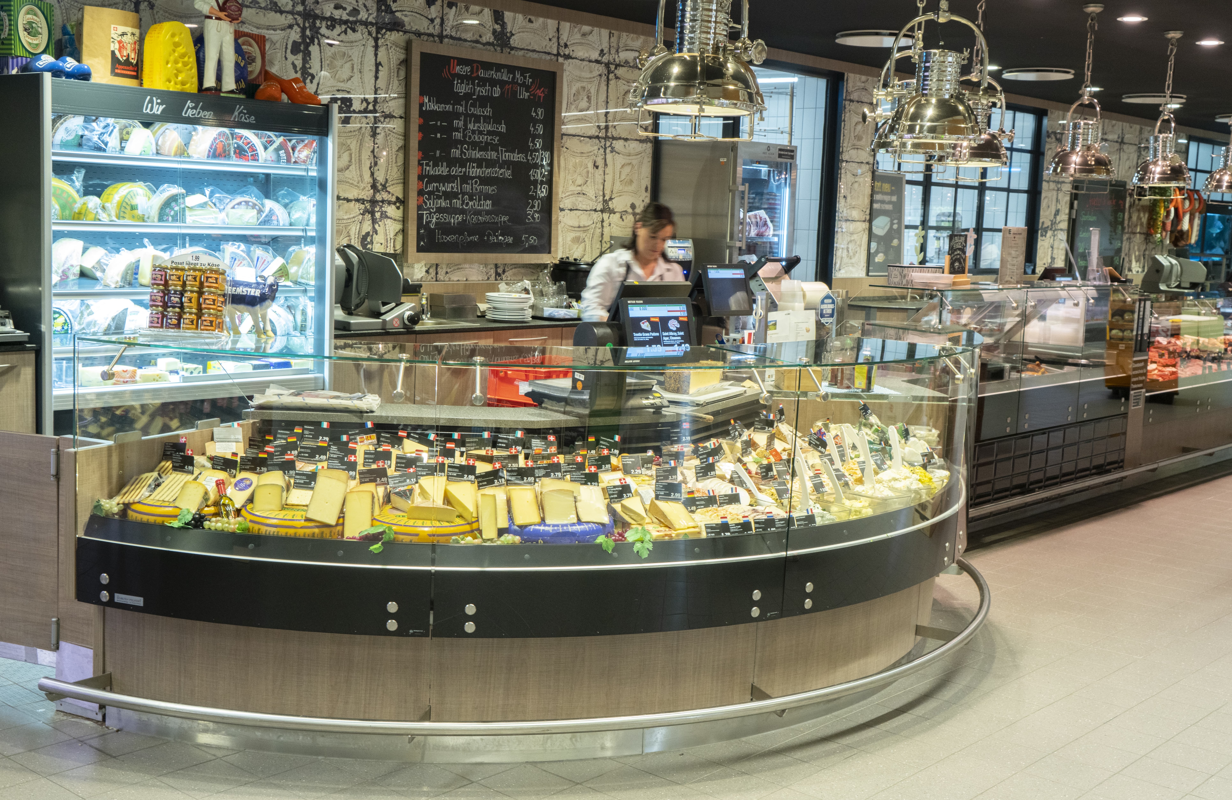 Hinter der rundlichen Käsetheke steht eine Mitarbeiterin an der Kasse.