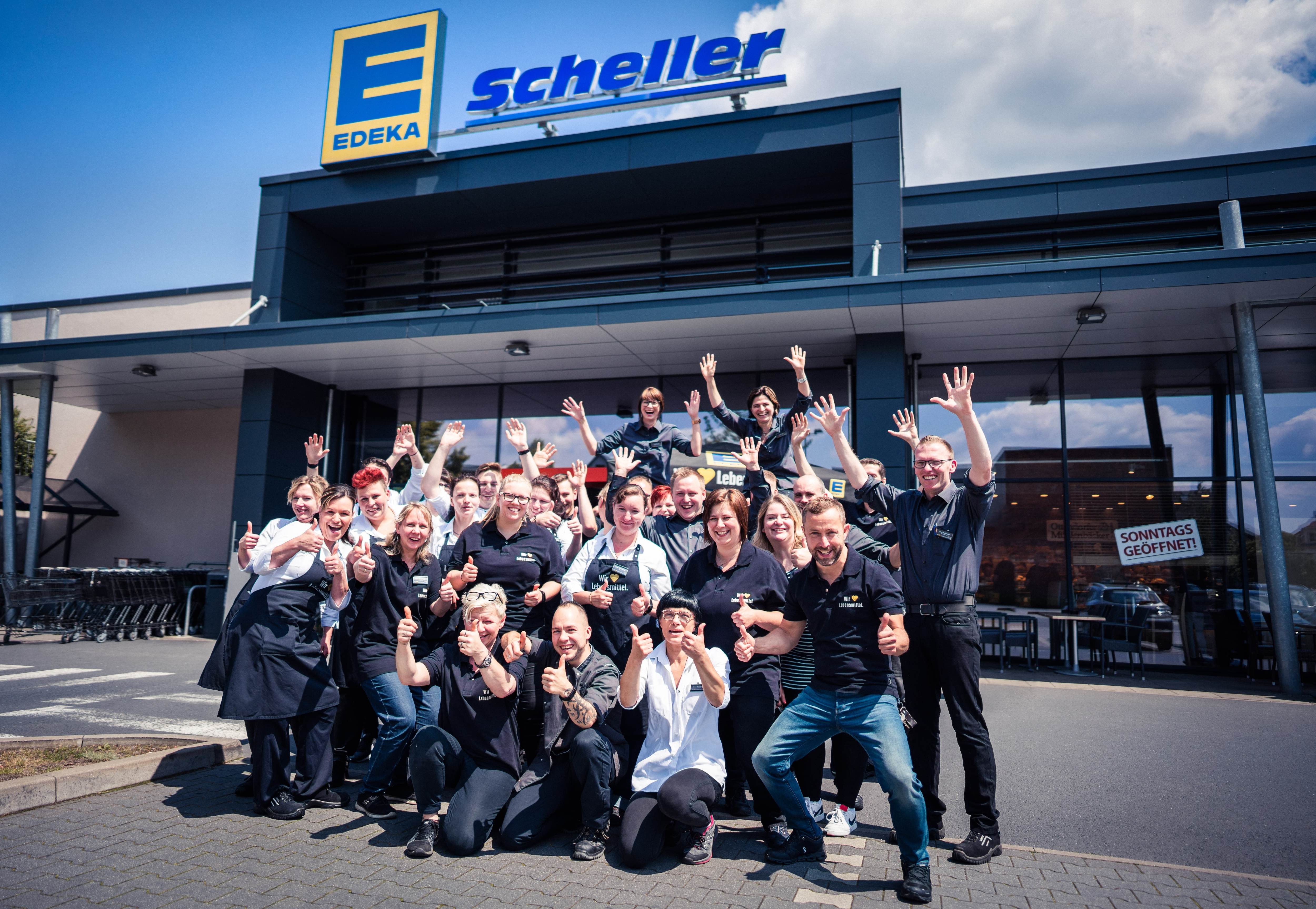 Gruppenbild mit winkenden Mitarbeiterinnen und Mitarbeitern vor EDEKA Scheller.
