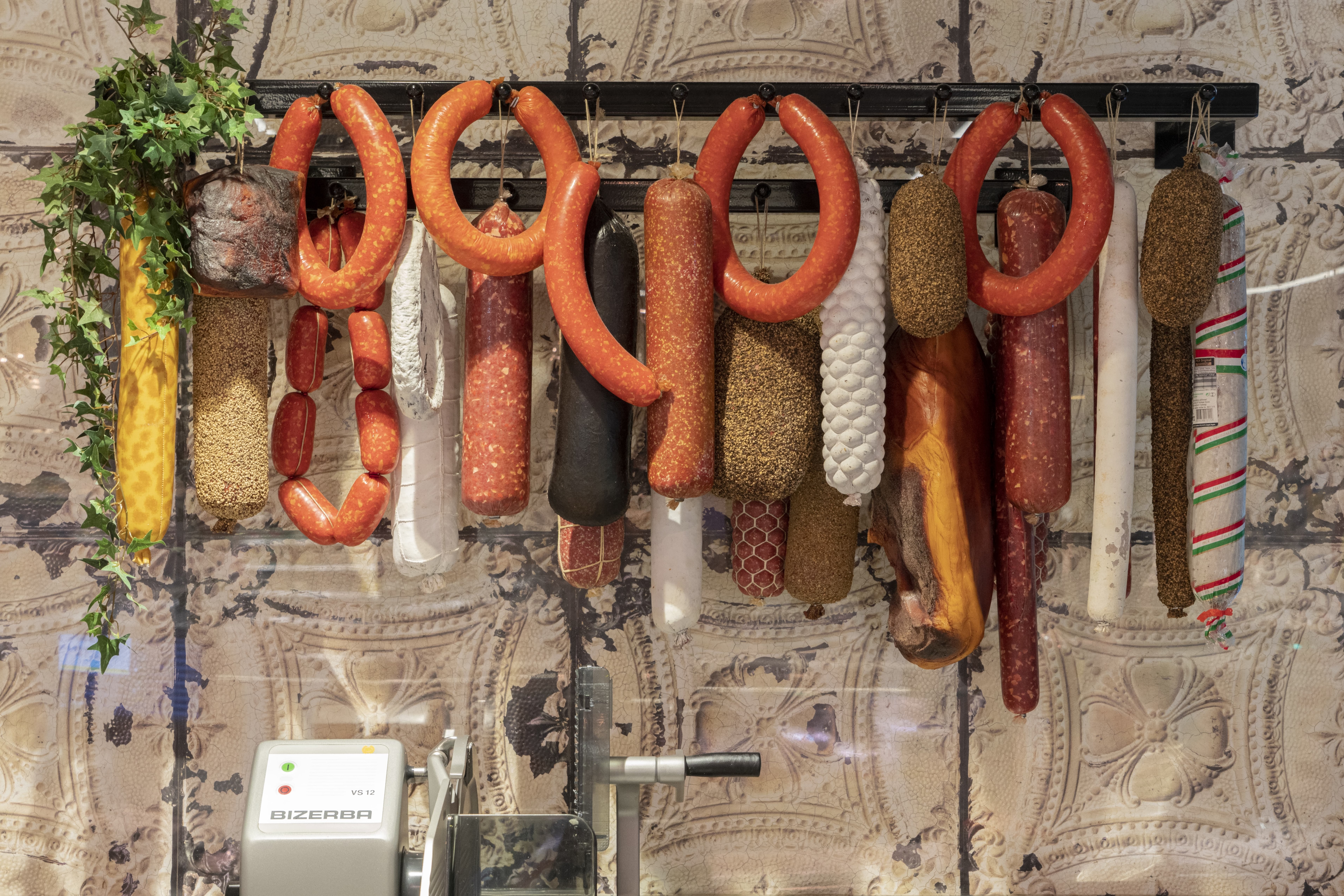 An Schnuren hängen Räucherwürste an einer Halterung hinter dem Tresen.