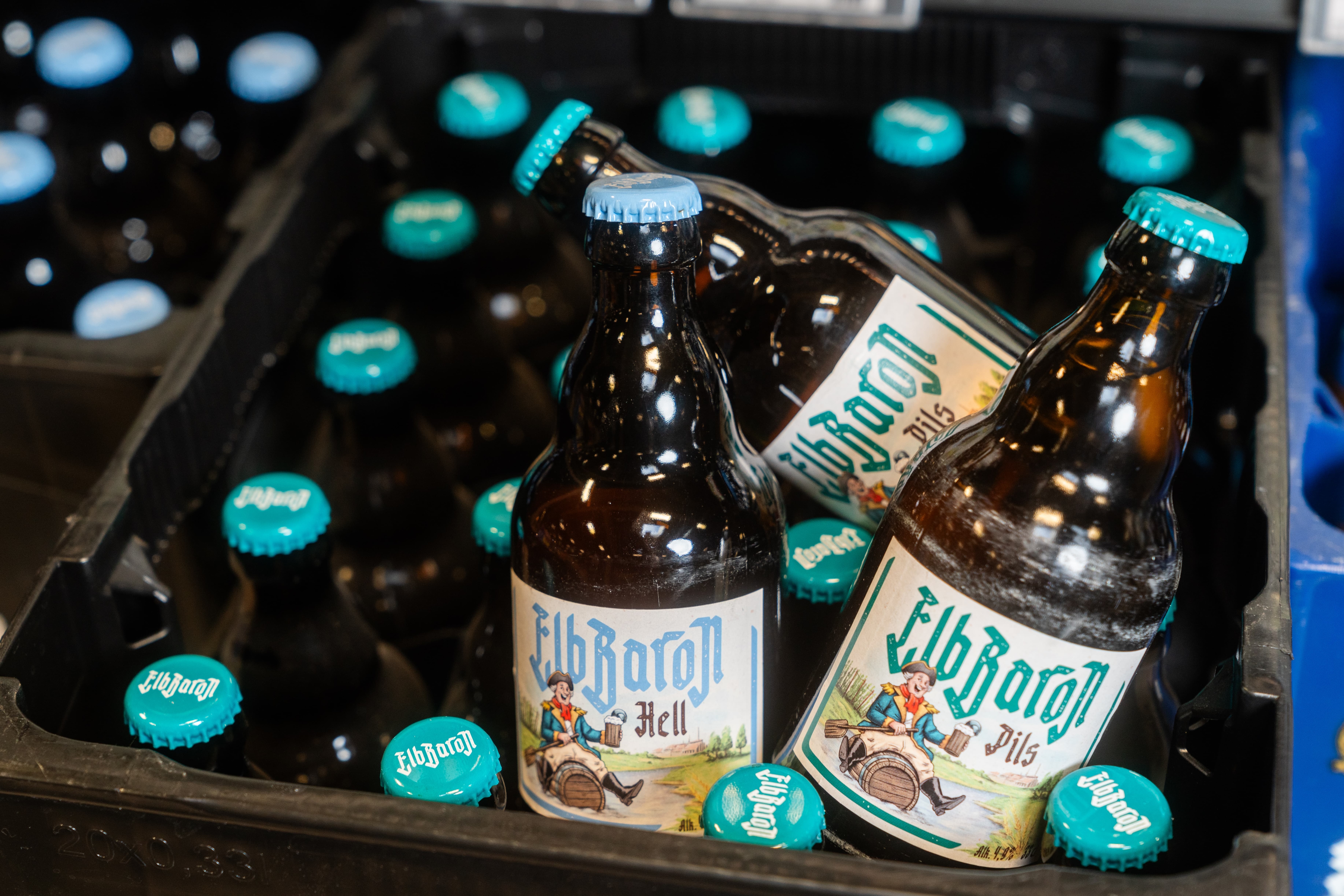 Drei Bierflaschen der Marke ElbBaron liegen auf einer schwarzen Bierkiste der selben Marke.