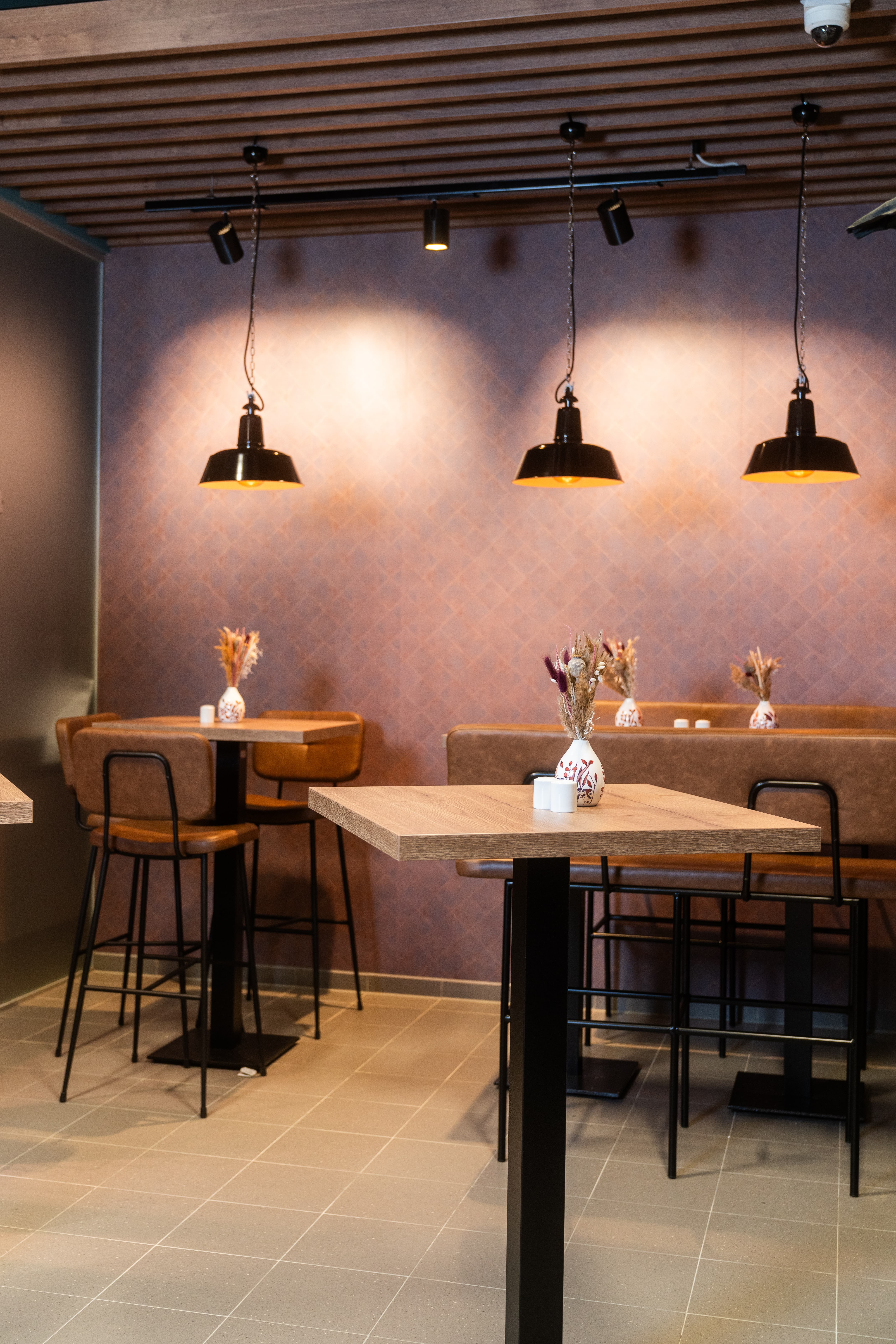 Stehtische mit Barhockern und einer erhöhten Bank. Warmes Licht strahlt aus Deckenlampen.