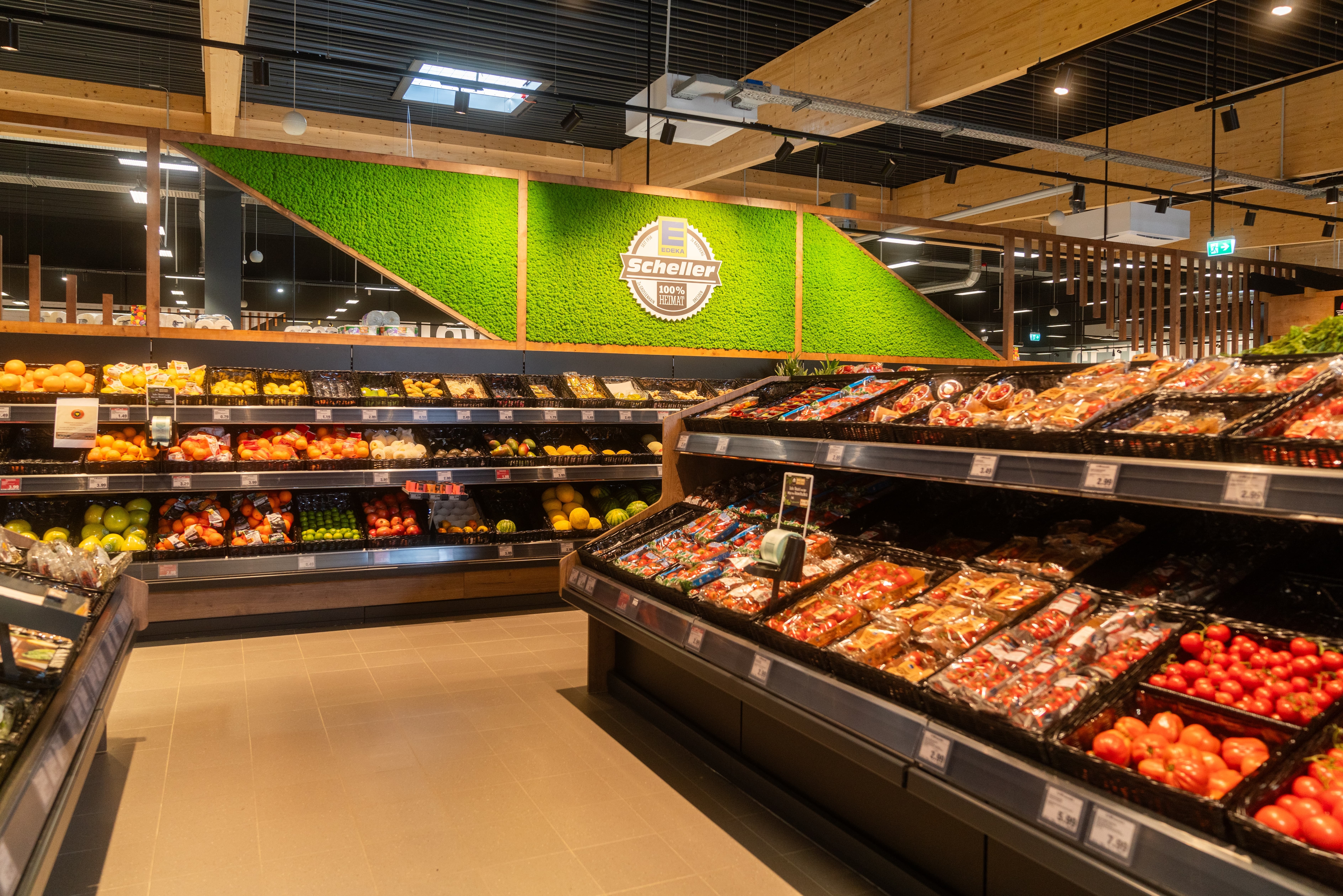 Gemüseabteilung mit dreistöckigen Regalen. An der Wand sind beleuchtete Moos-Elemente und das EDEKA-Scheller-Logo.