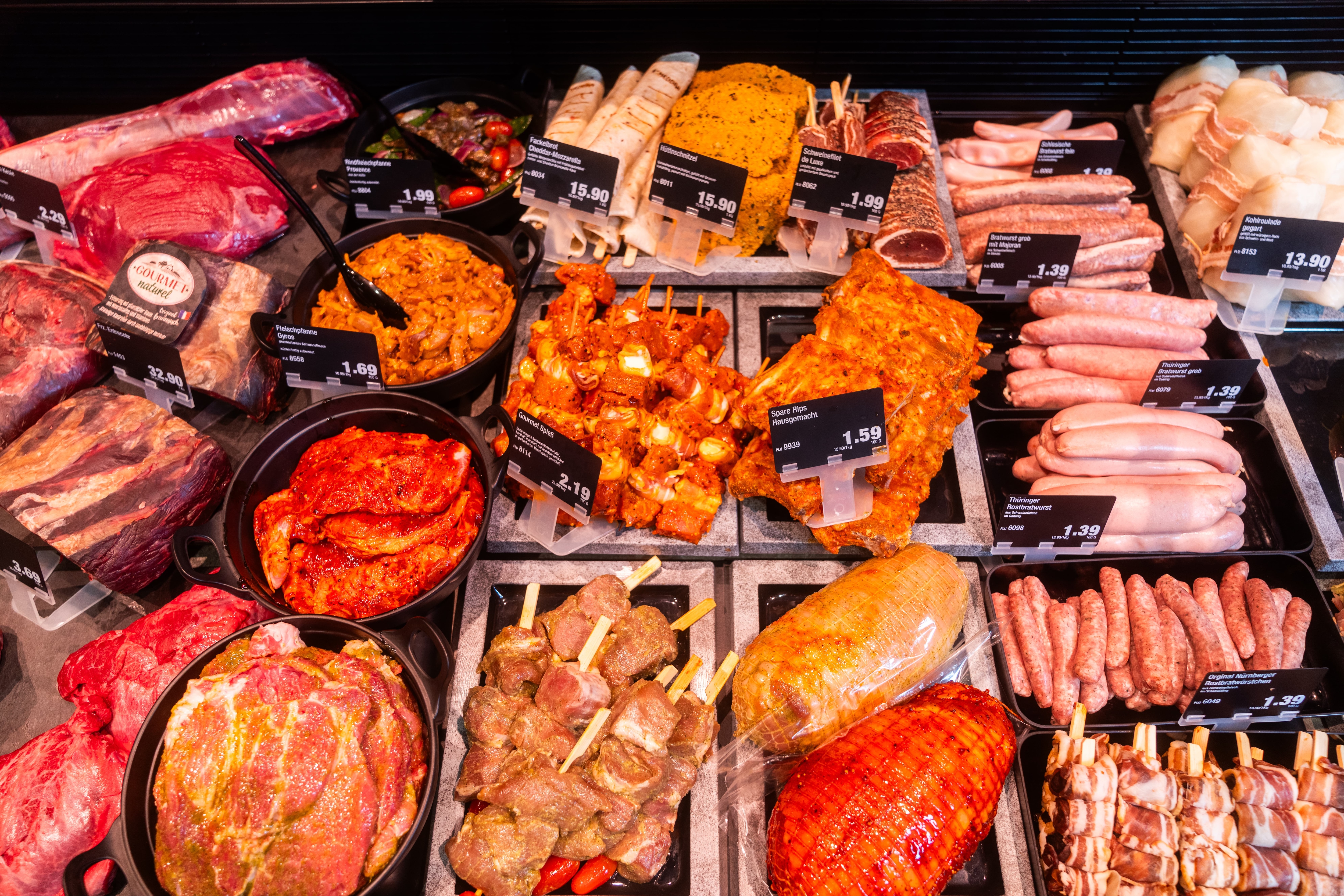 Mariniertes Grillfleisch und Würste mit Preisschildern.