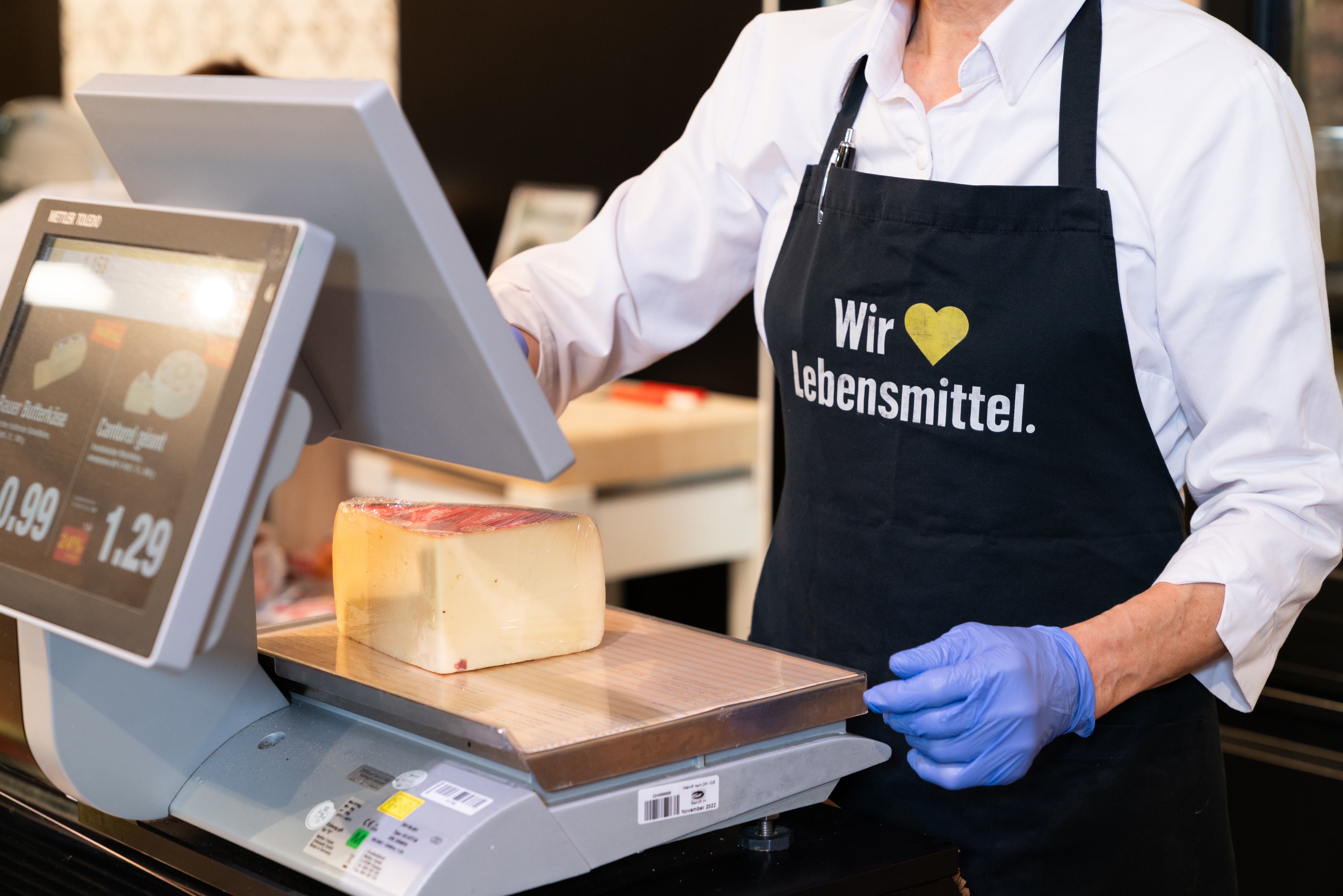 An der Käsewaage steht eine Person mit schwarzer EDEKA-Schürze.