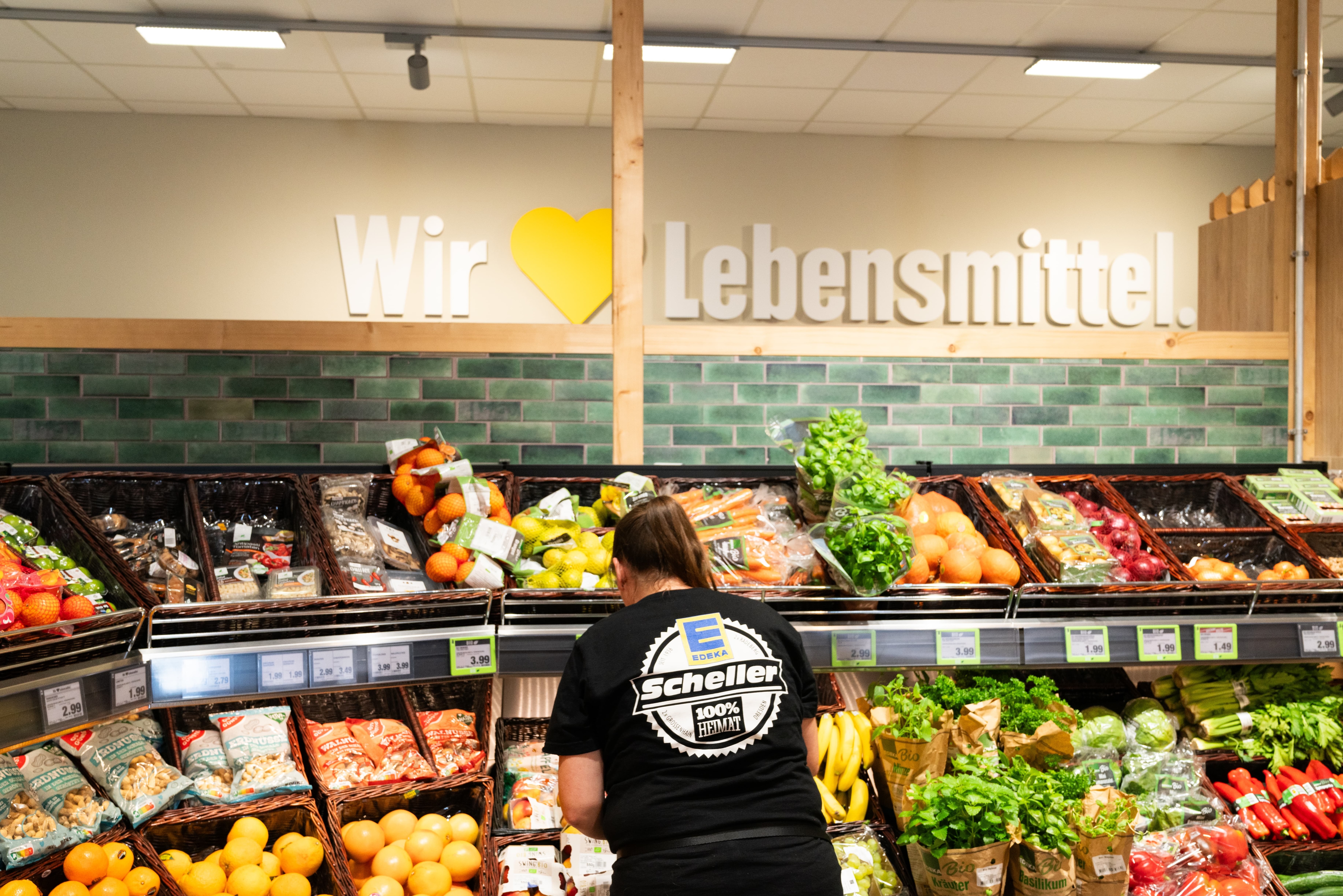 Eine Frau mit schwarzem EDEKA-T-Shirt steht am Obstregal, über dem Wir lieben Lebensmittel steht.