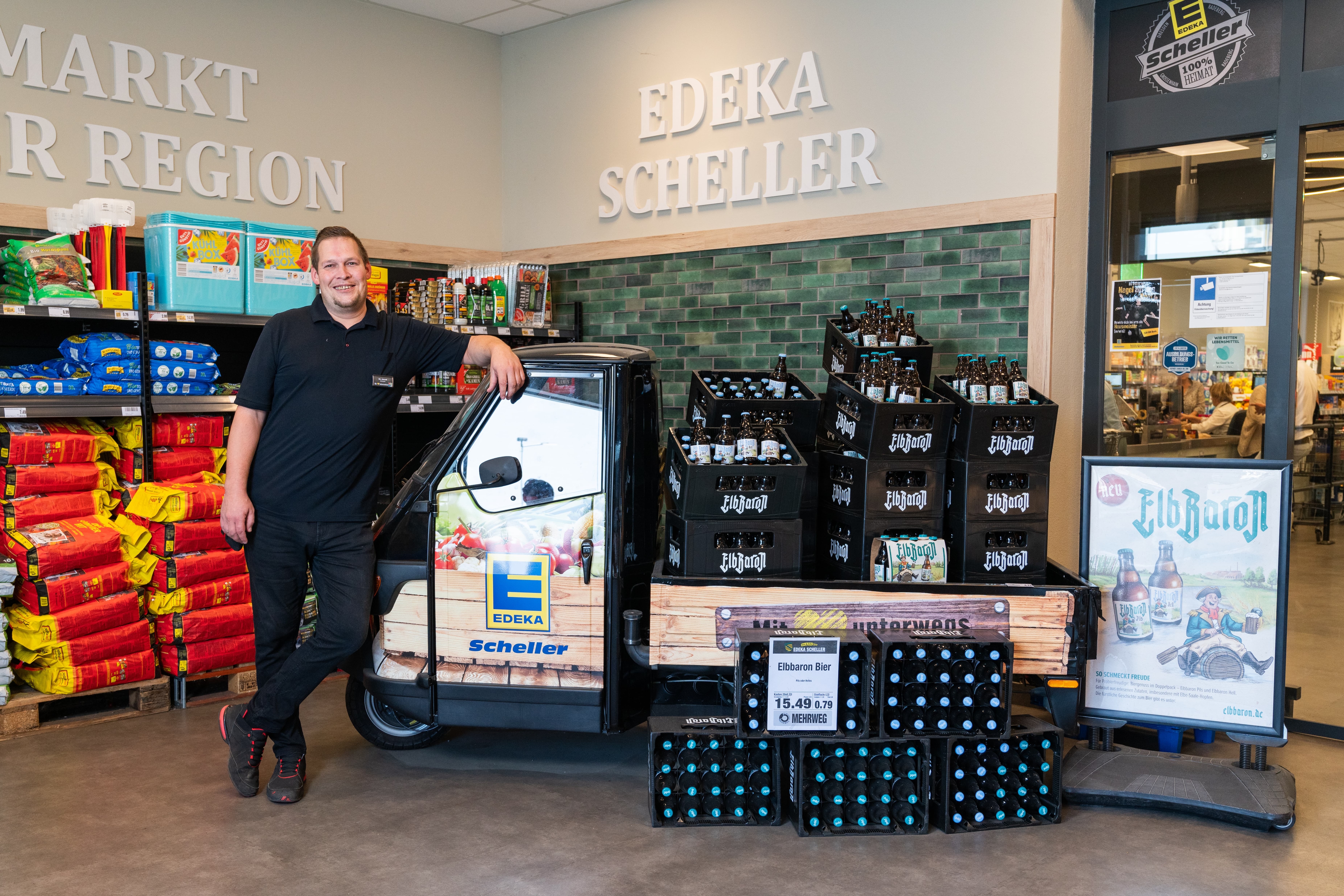 Ein Mann lehnt an einem kleinen Fahrzeug mit Bierkisten auf der Ladefläche.