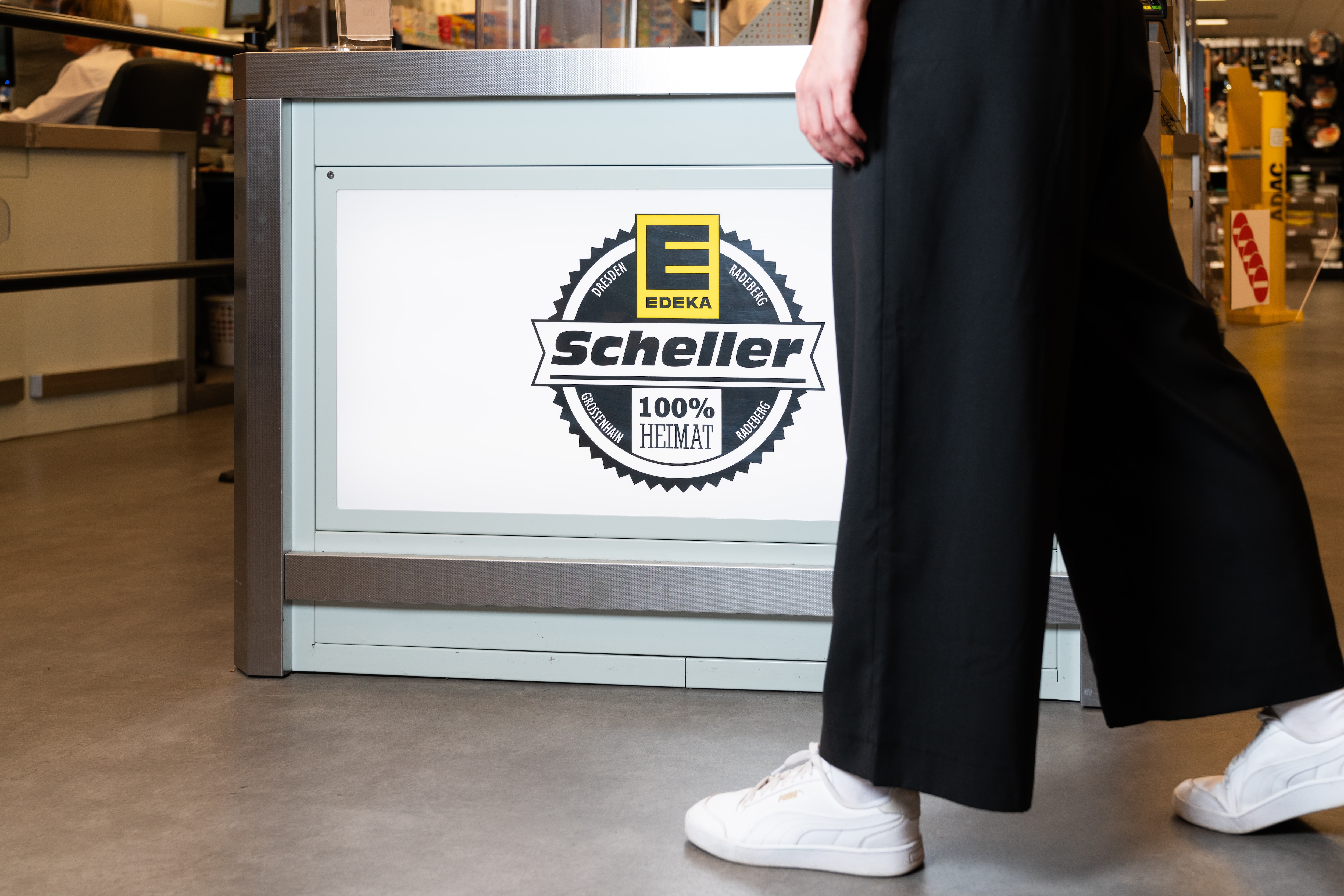 Das Logo von EDEKA Scheller an der Rückseite des Kassenbereichs.