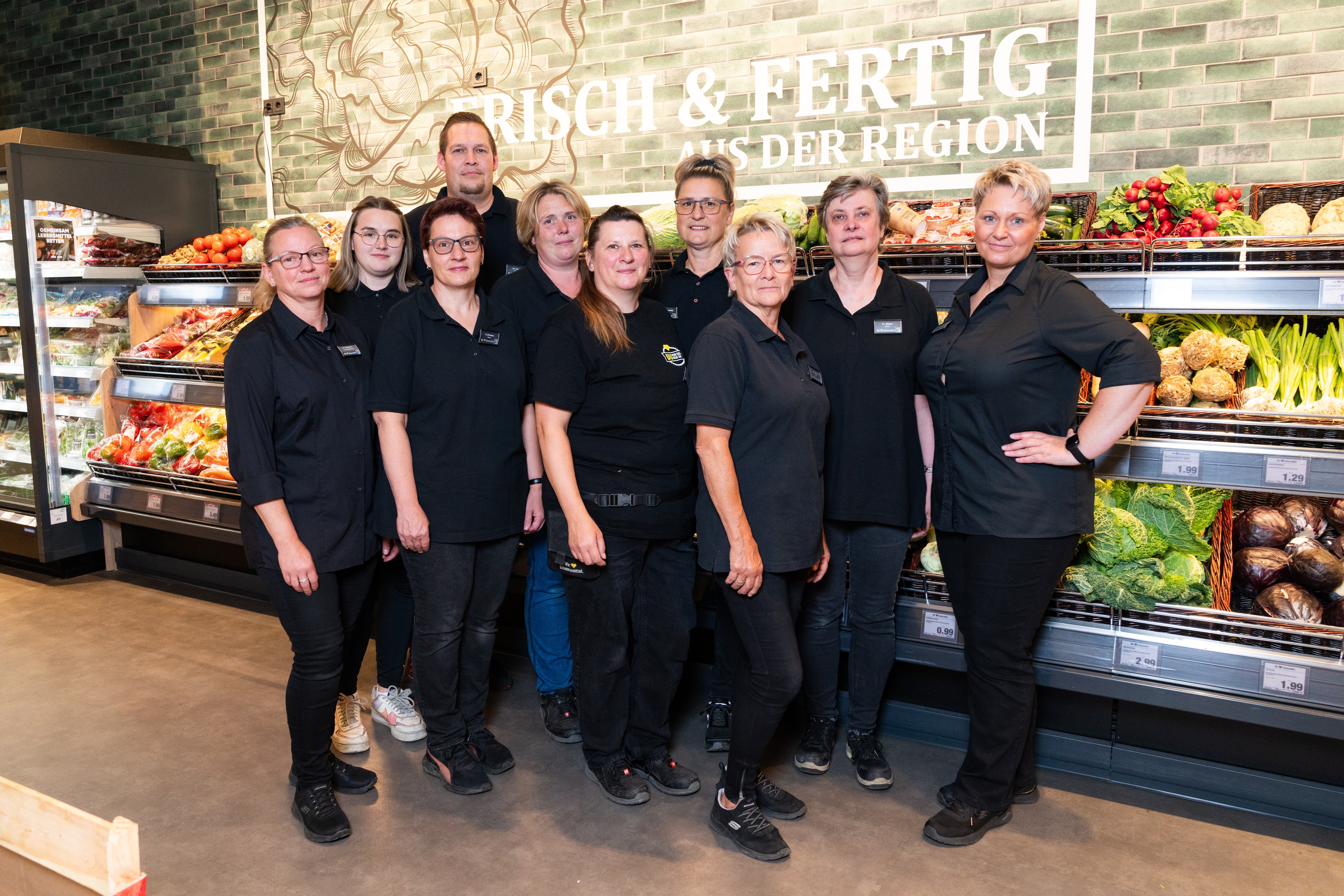 Zehn Erwachsene in schwarzer Kleidung posieren vor der Gemüseabteilung.
