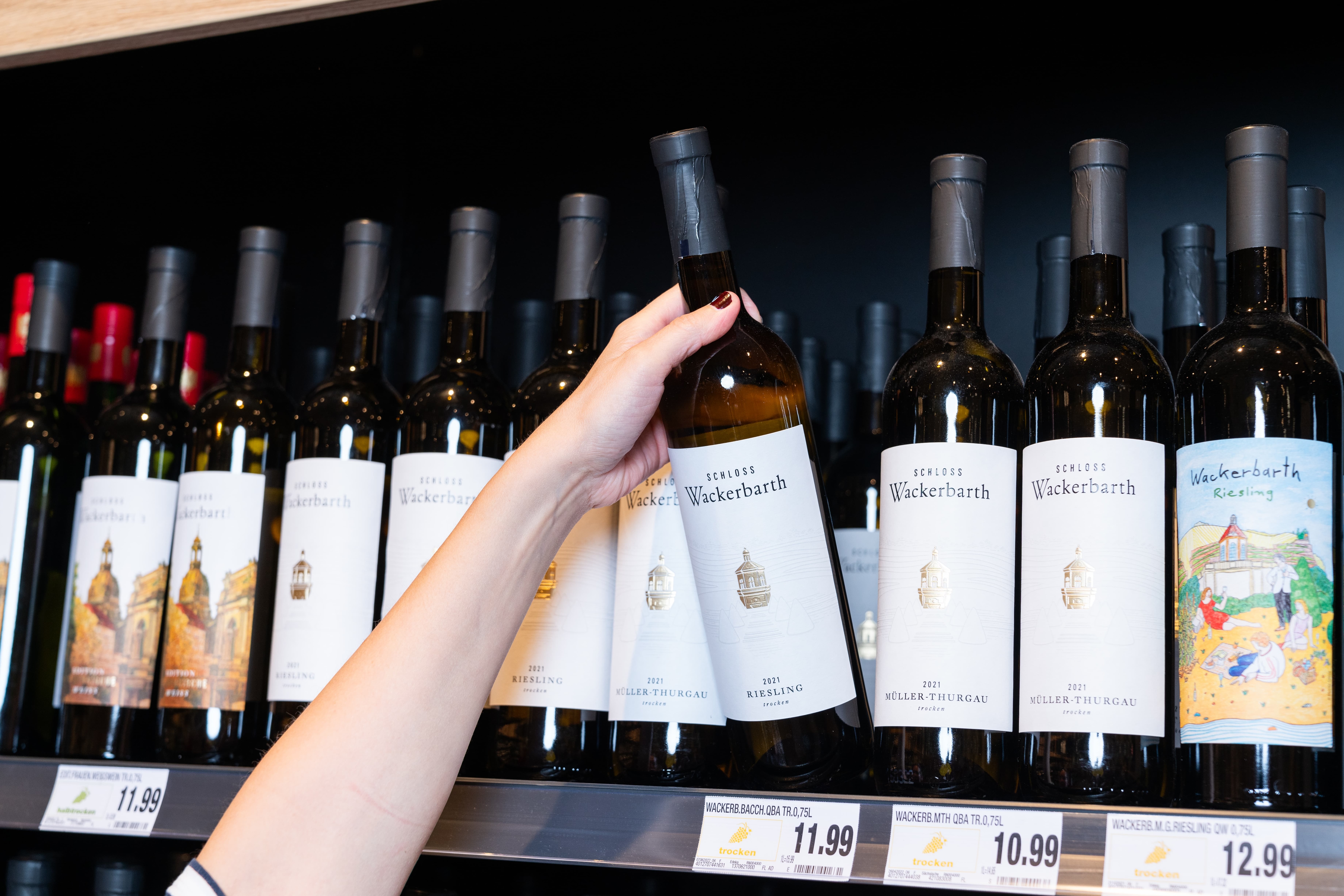 Eine weibliche Hand greift nach einer Flasche Wein. Auf dem Etikett steht Schloss Wackerbarth Riesling.