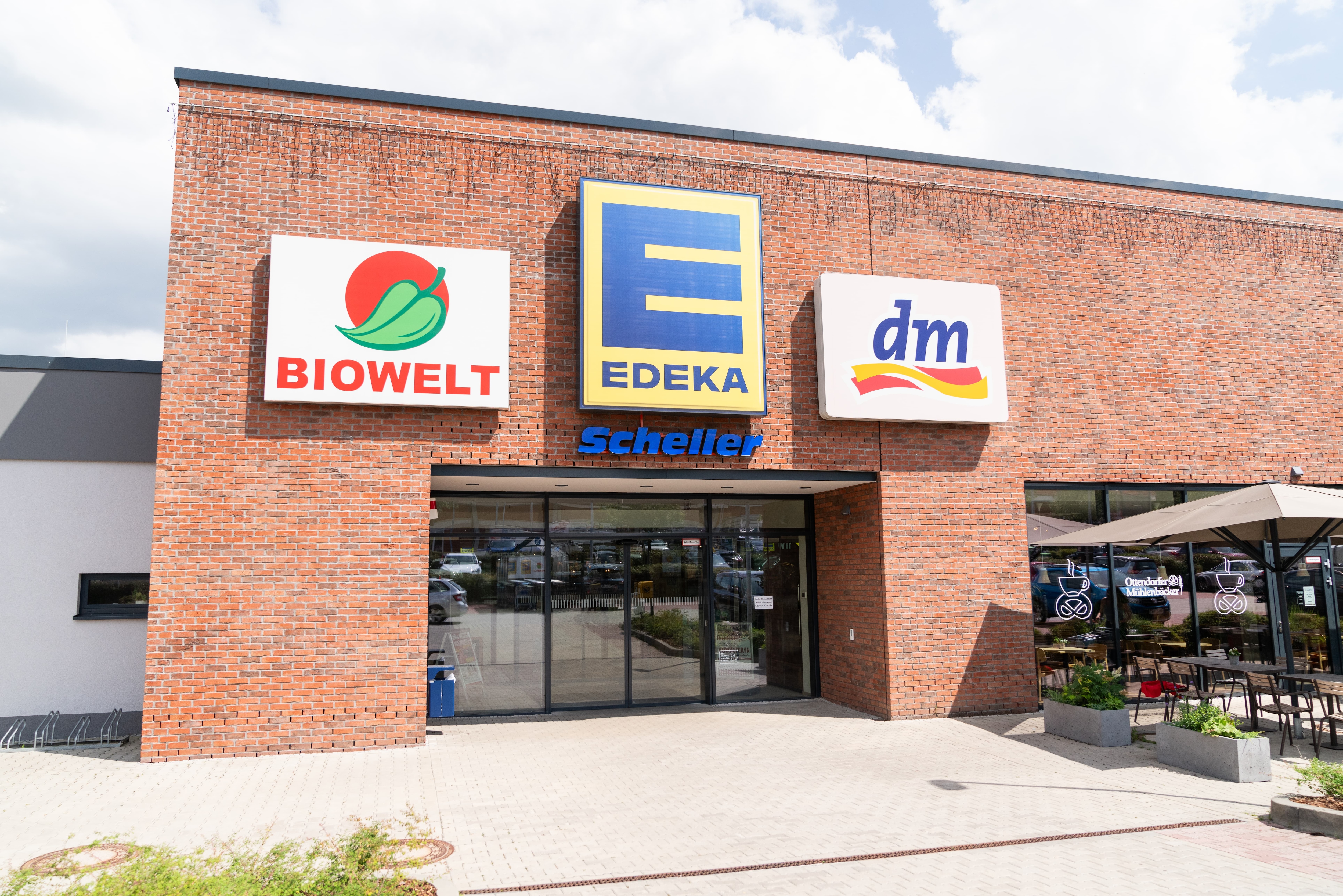 EDEKA Scheller von außen mit hellroten Mauersteinen. Das EDEKA-Logo steht zwischen den Logos von Biowelt und dm.