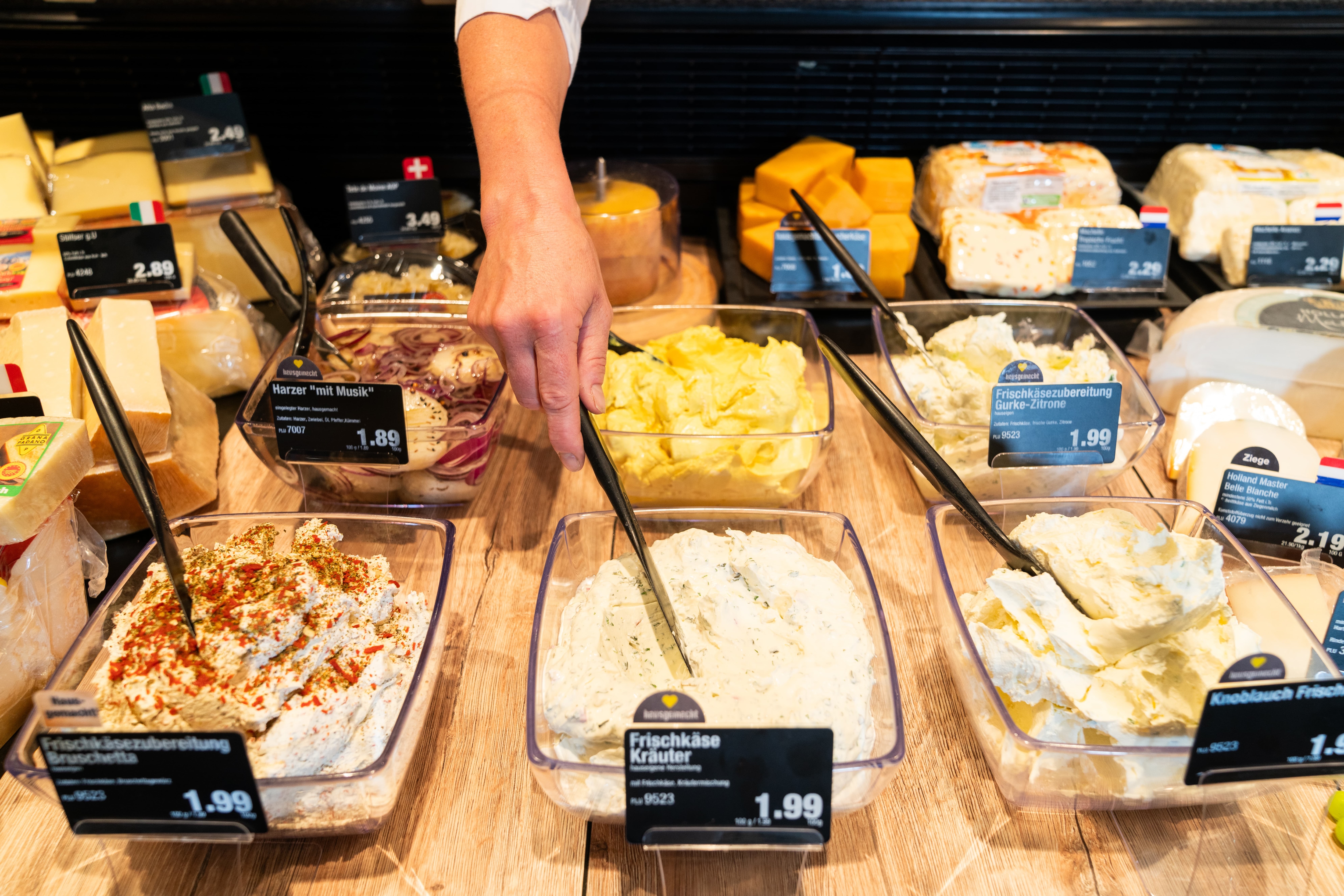 Eine Hand steckt einen Löffel in eine Schüssel mit der Beschriftung Frischkäse Kräuter.