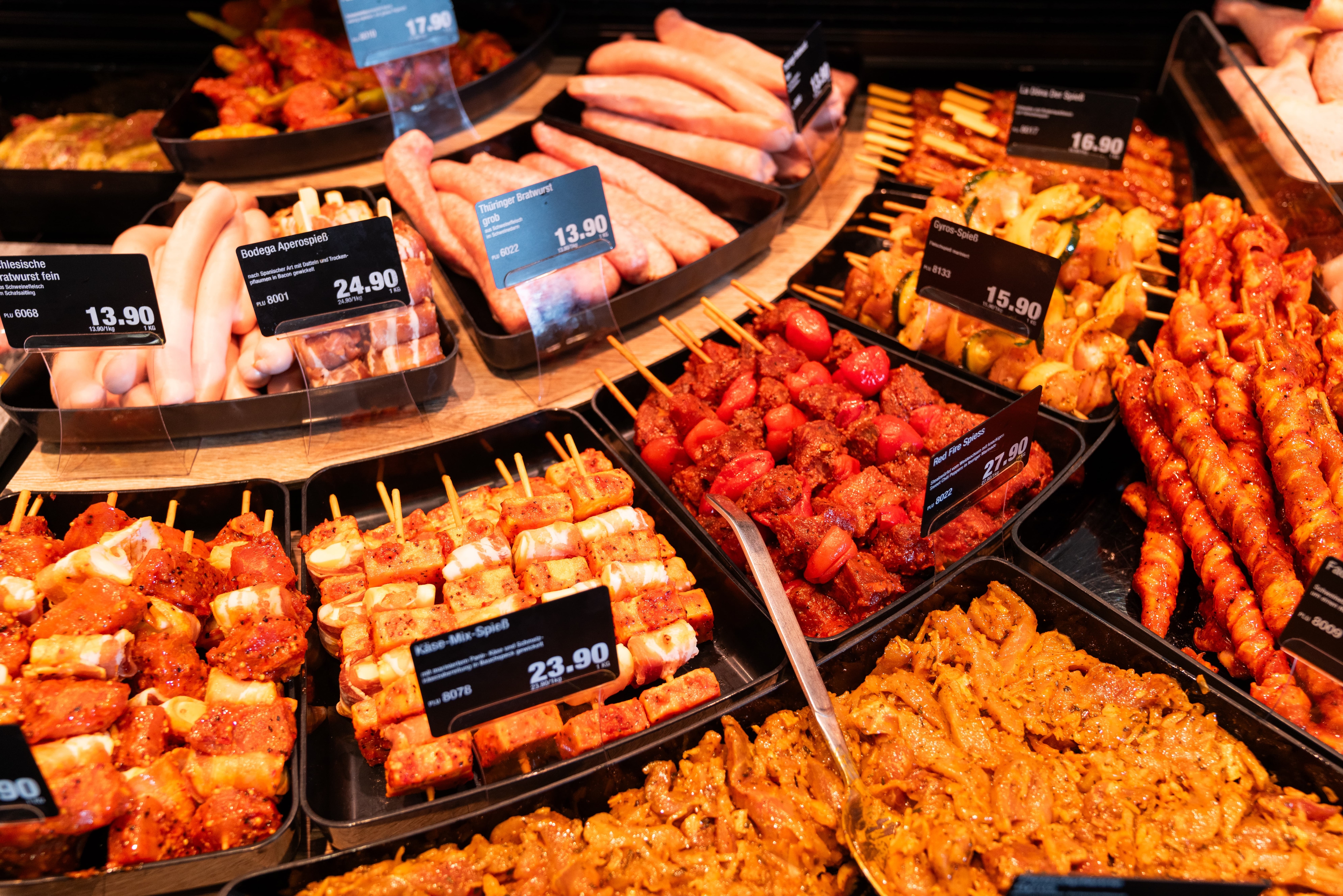 Marinierte Fleischspieße in schwarzen Schalen mit Preisschildern.