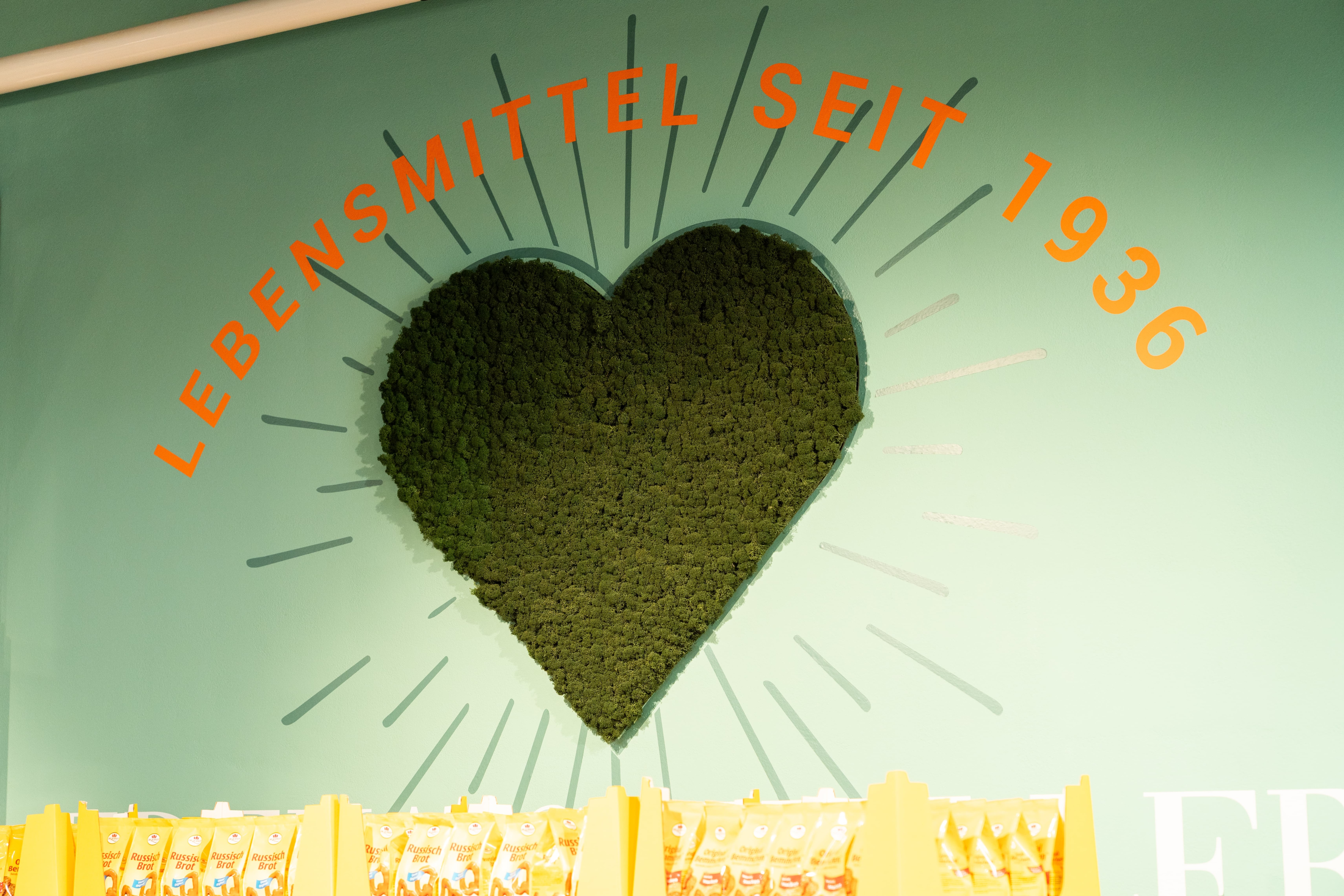 An einer Wand hängt ein großes grünes Herz aus Moos. Darüber steht Lebensmittel seit 1936.