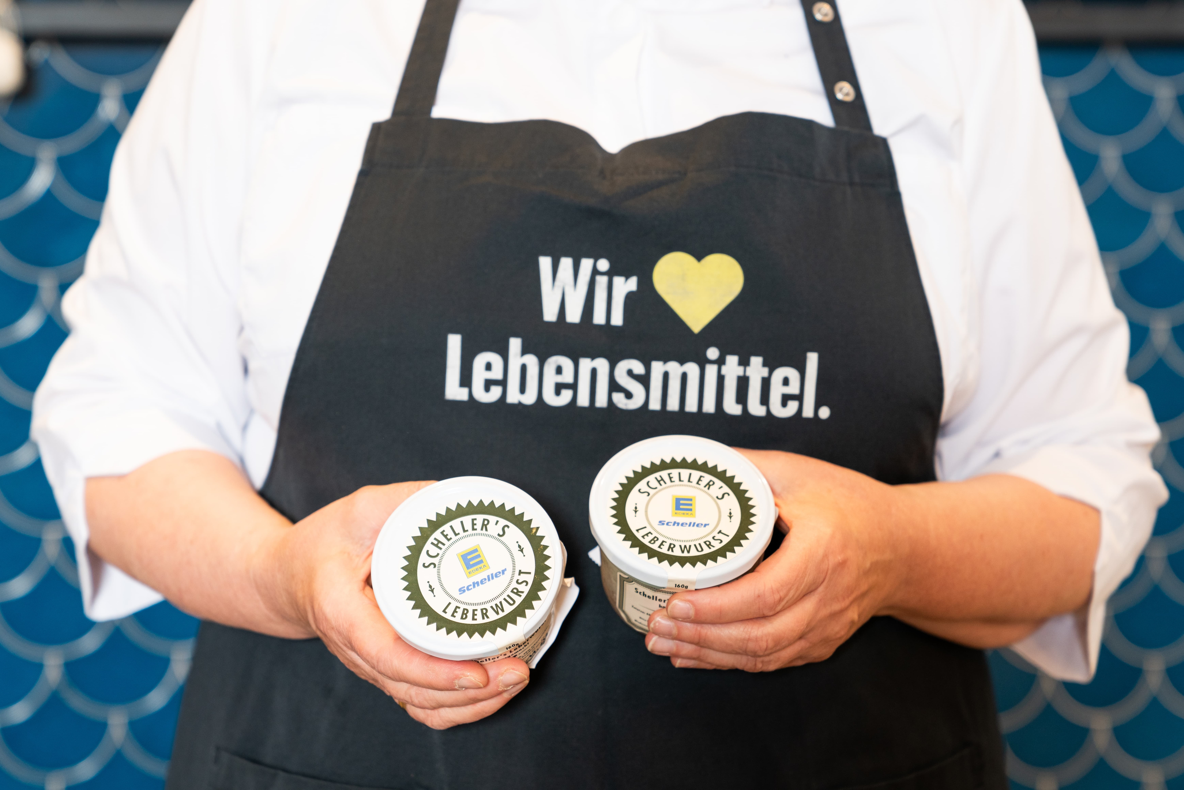 Eine Person mit einer schwarzen EDEKA-Schürze hält zwei Gläser Scheller´s Leberwurst in den Händen.