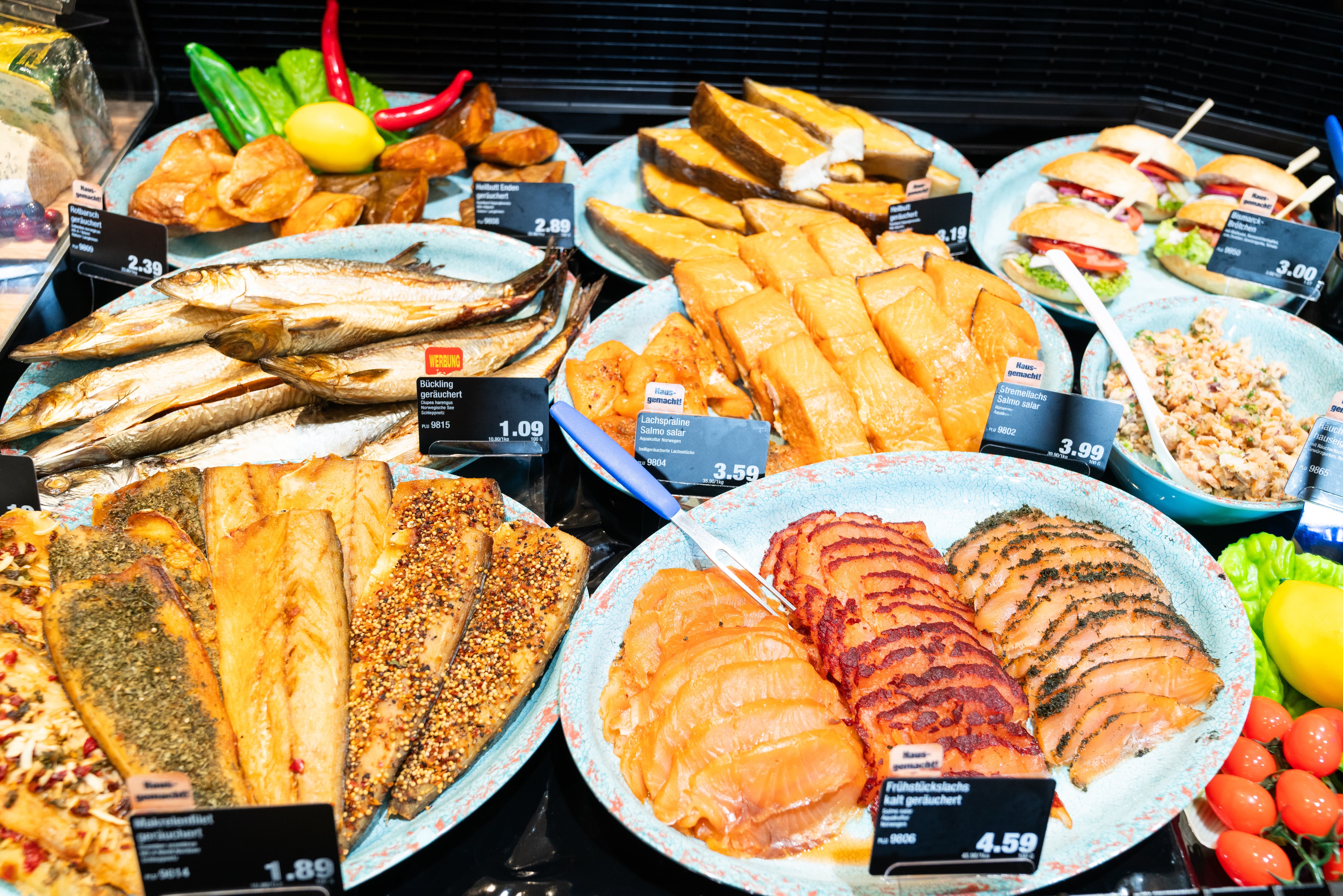 Räucherfisch auf hellblauen Tellern mit Preisschildern.