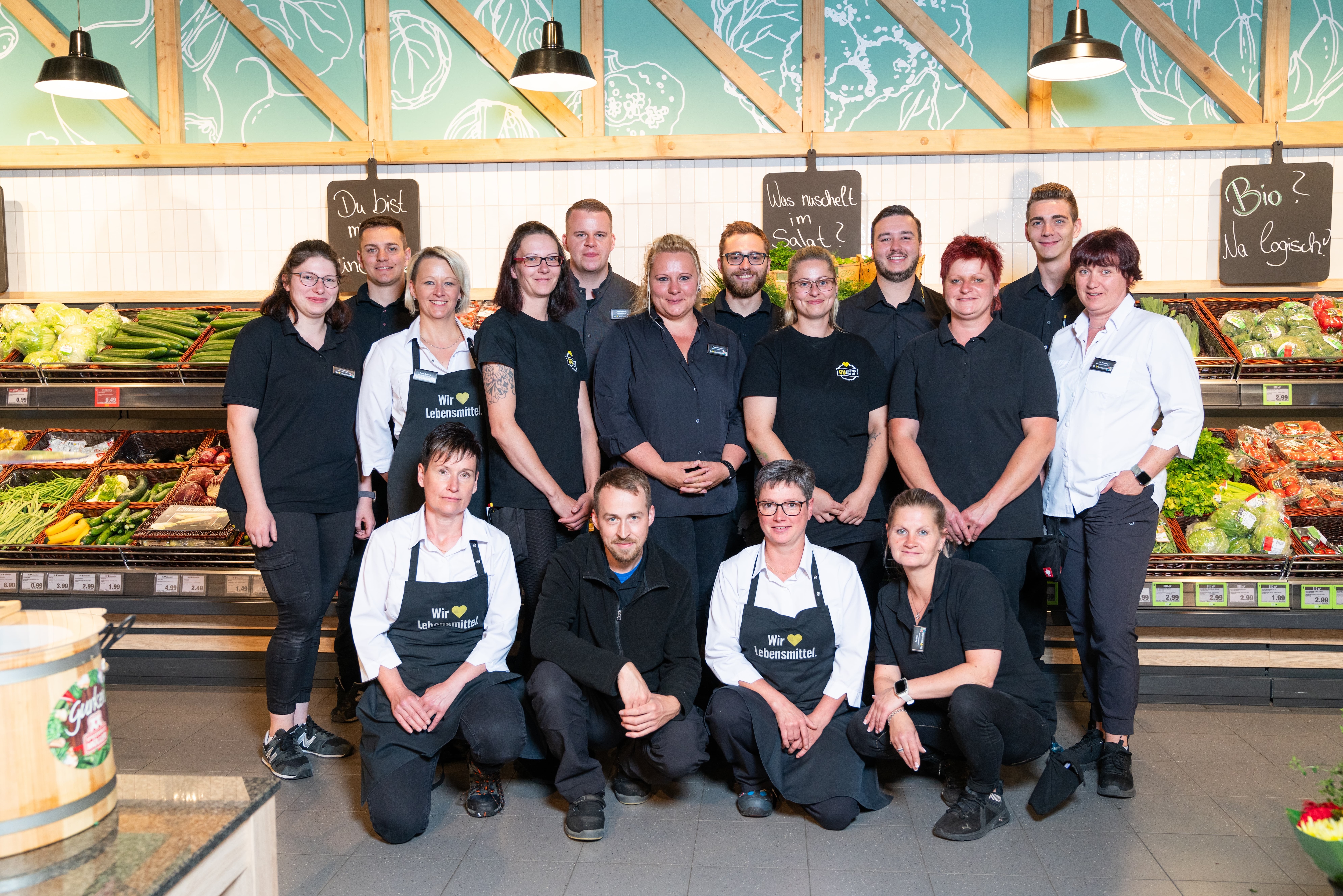 16 Personen in EDEKA-Kleidung stehen vor dem Gemüseregal.