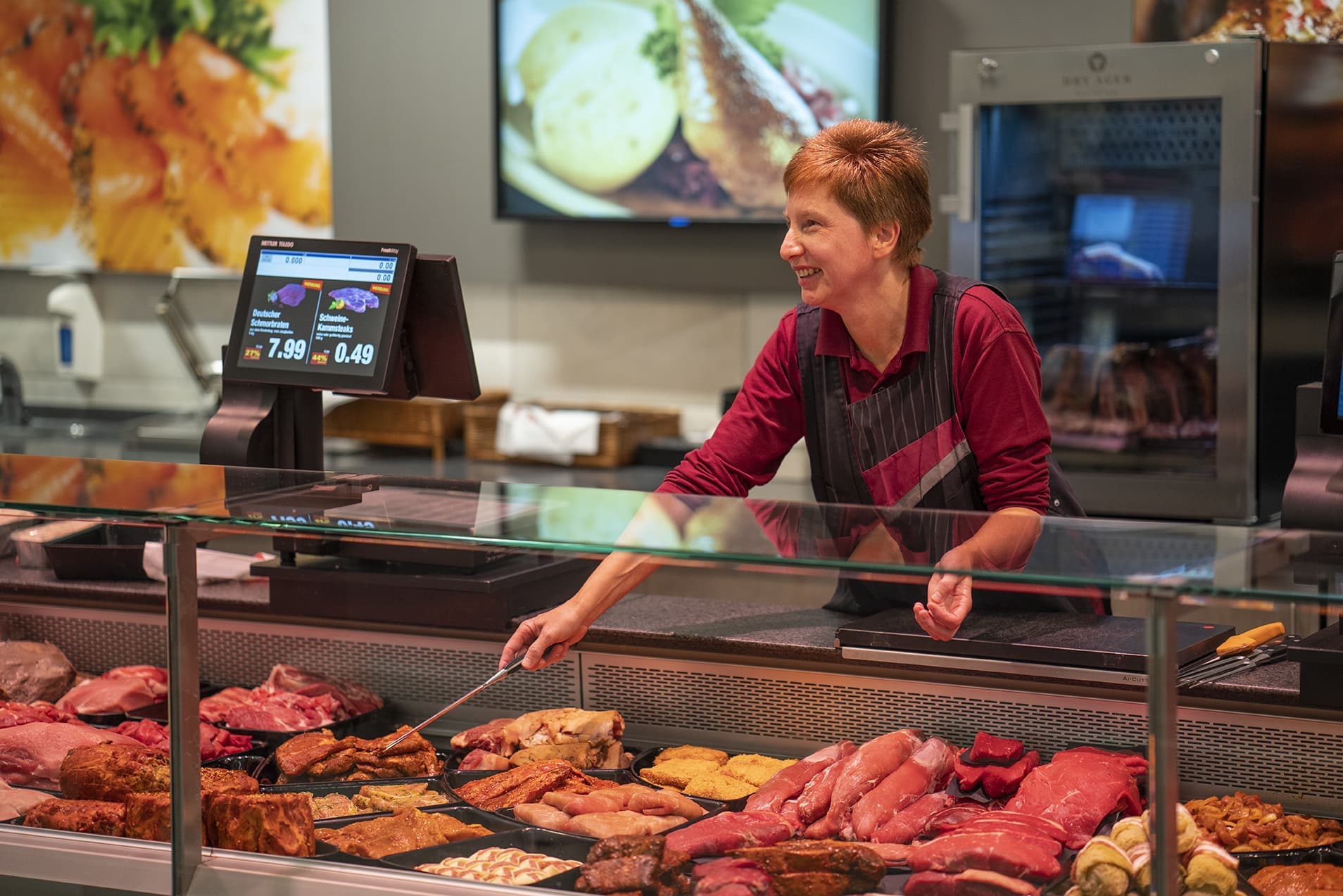Eine Mitarbeiterin an der Bedientheke lächelt jemanden an, der nicht im Bild zu sehen ist.