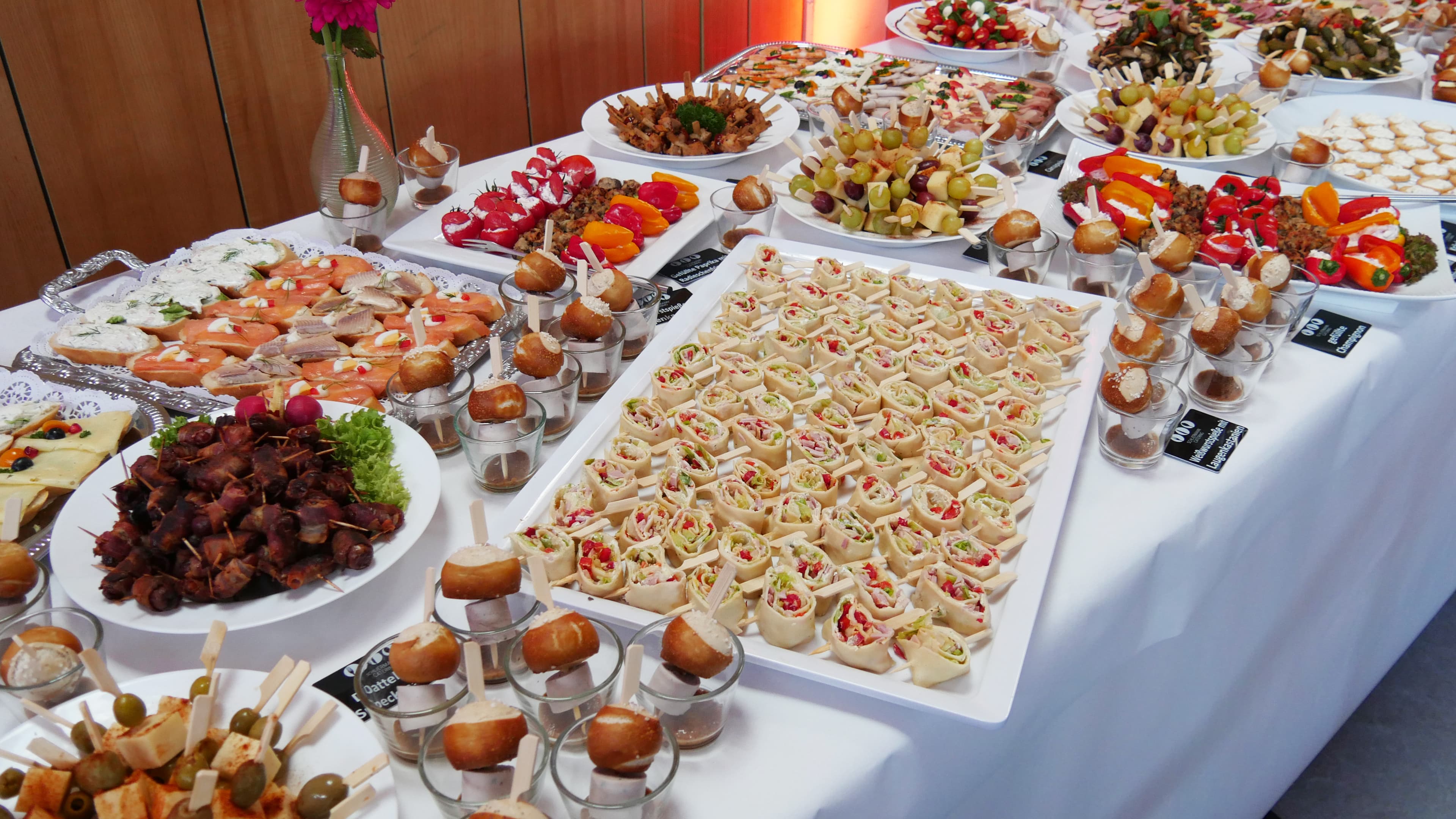 Ein reich gedecktes Buffet mit verschiedensten Sorten Fingerfood, darunter belegte Schnittchen, Brötchen, Spieße.