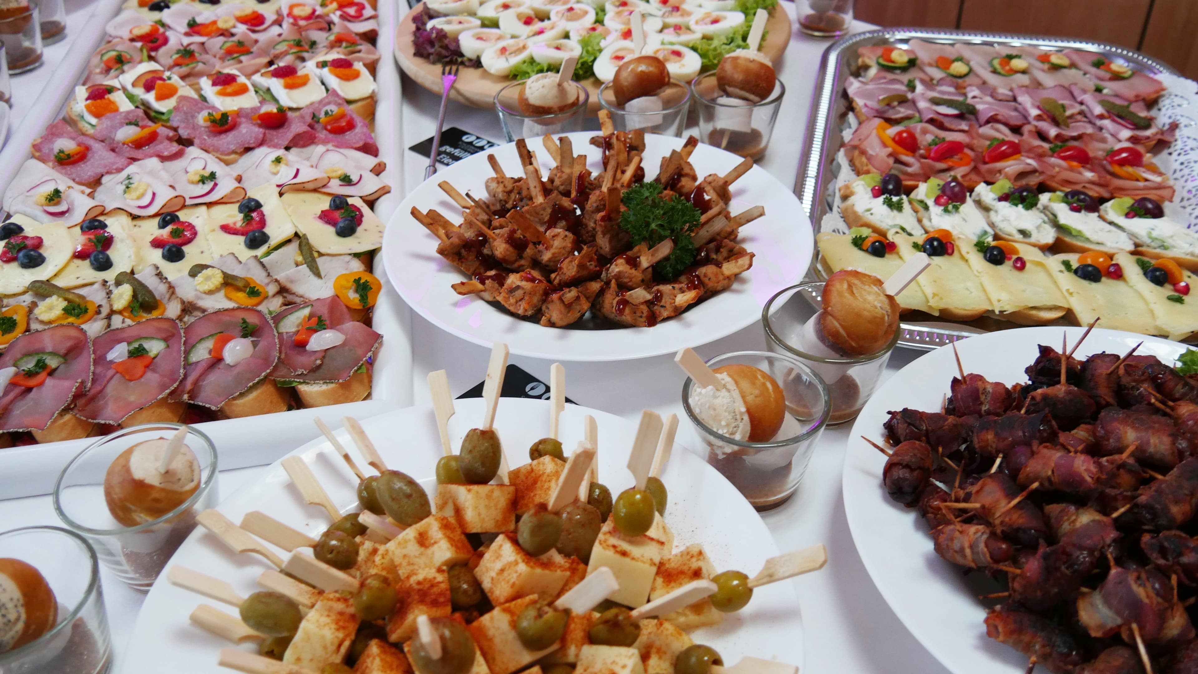 Ein reich gedecktes Buffet mit verschiedensten Sorten Fingerfood, darunter belegte Schnittchen, Brötchen, Spieße.