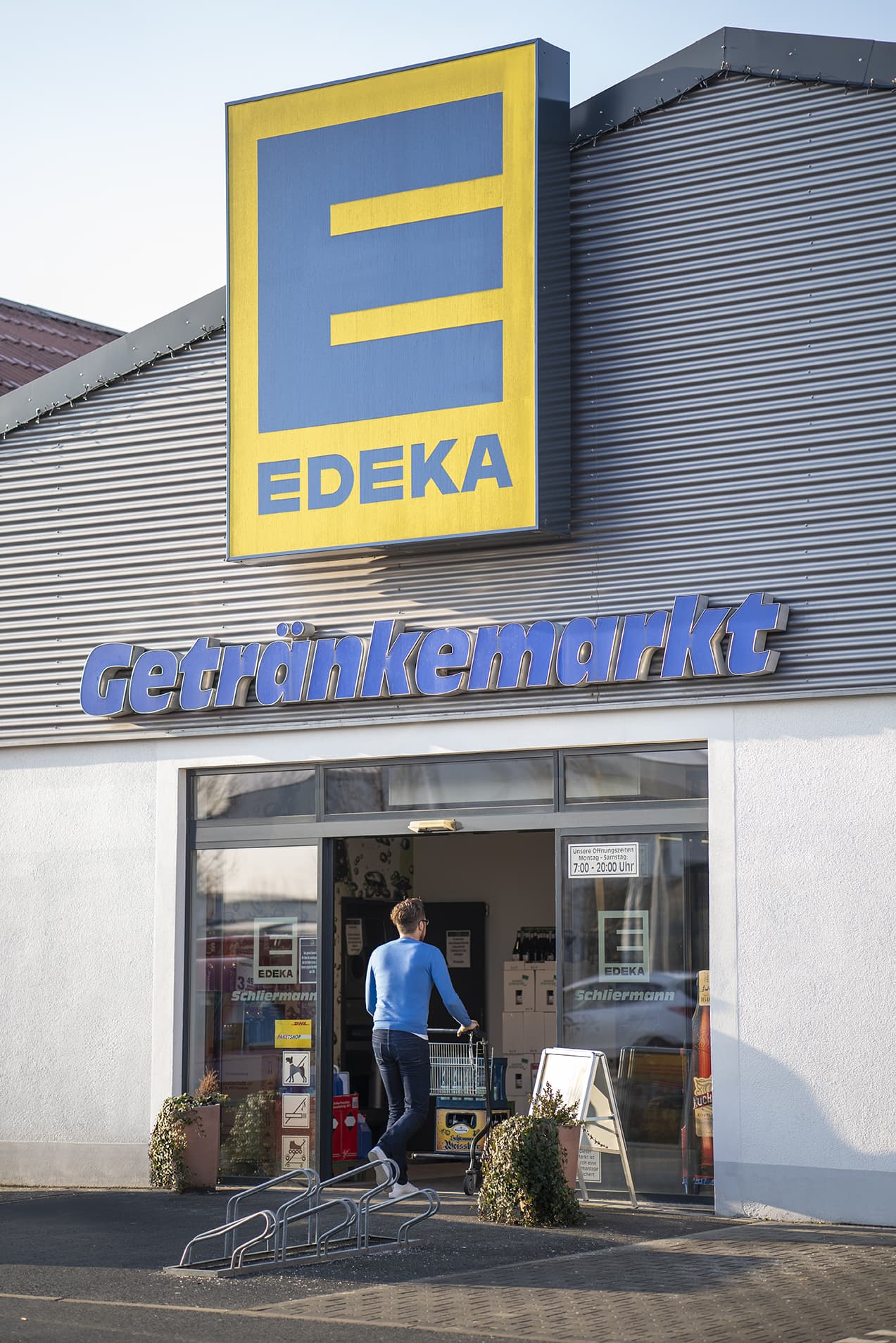 Front des Getränkemarkts, sonnenbeschienen. Ein Kunde fährt gerade einen Einkaufswagen hinein.