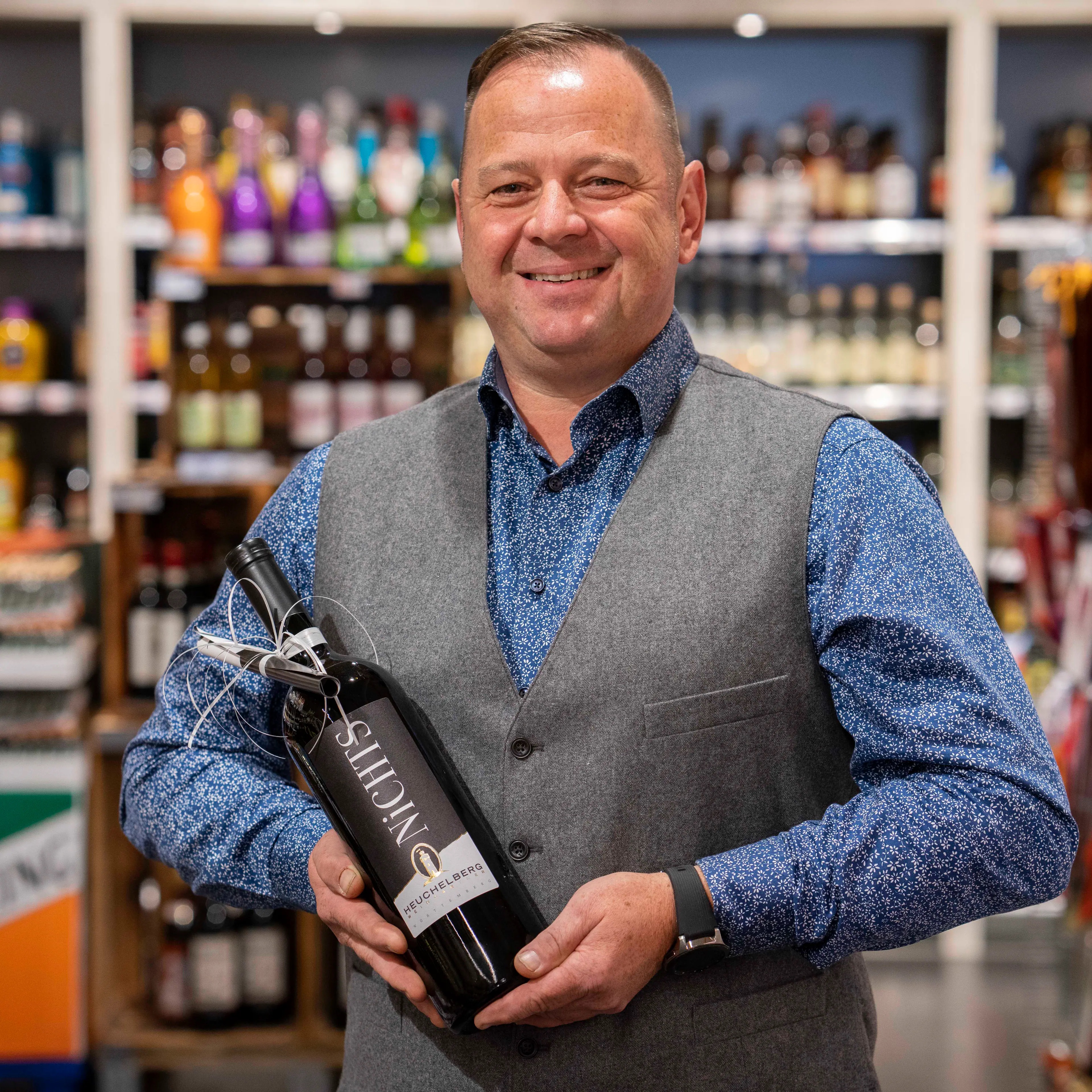 Der Marktleiter eines EDEKA-Marktes hält eine Flasche Wein in den Händen.