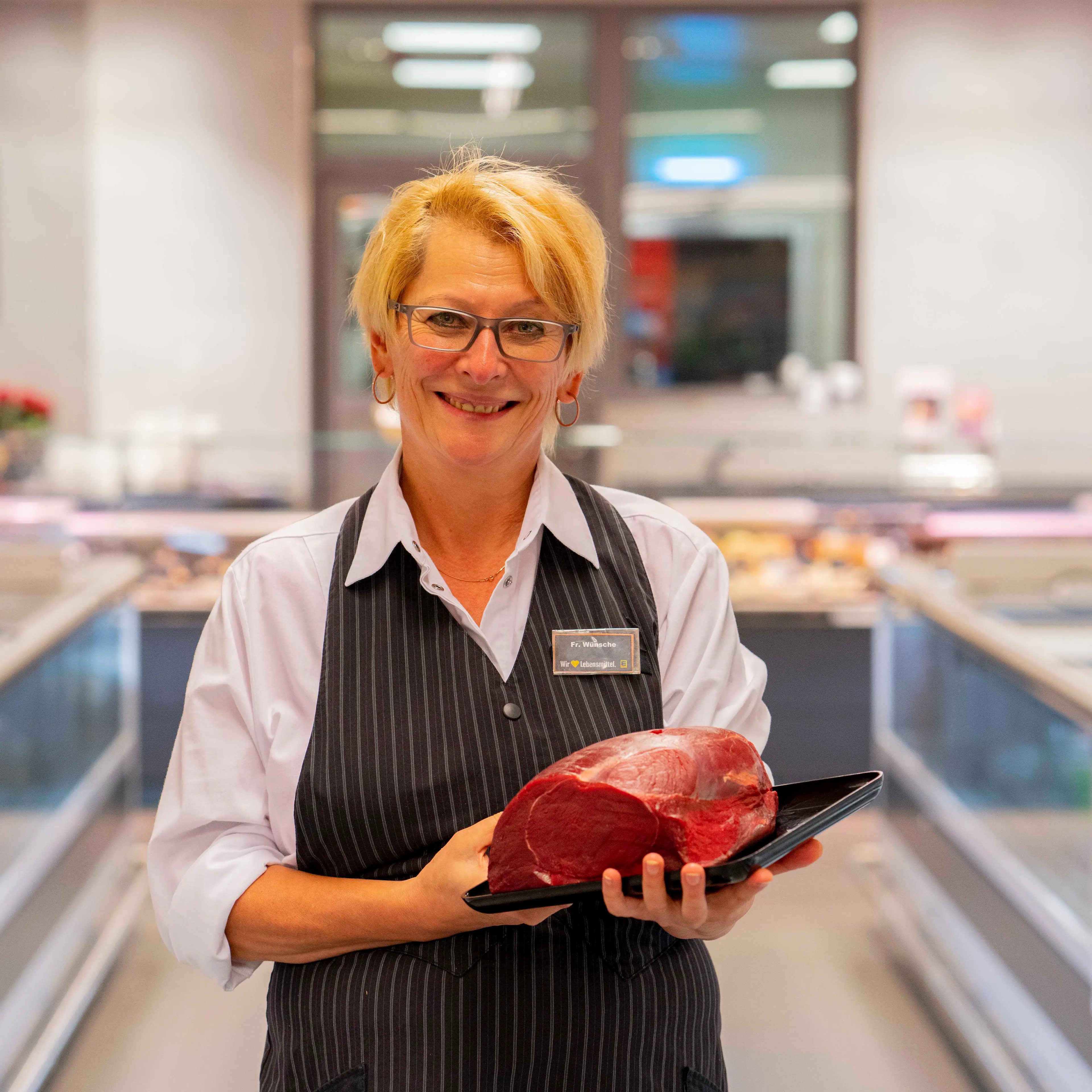 Eine lächelnde Mitarbeiterin halt eine Platte mit einem großen Stück Fleisch in den Händen.