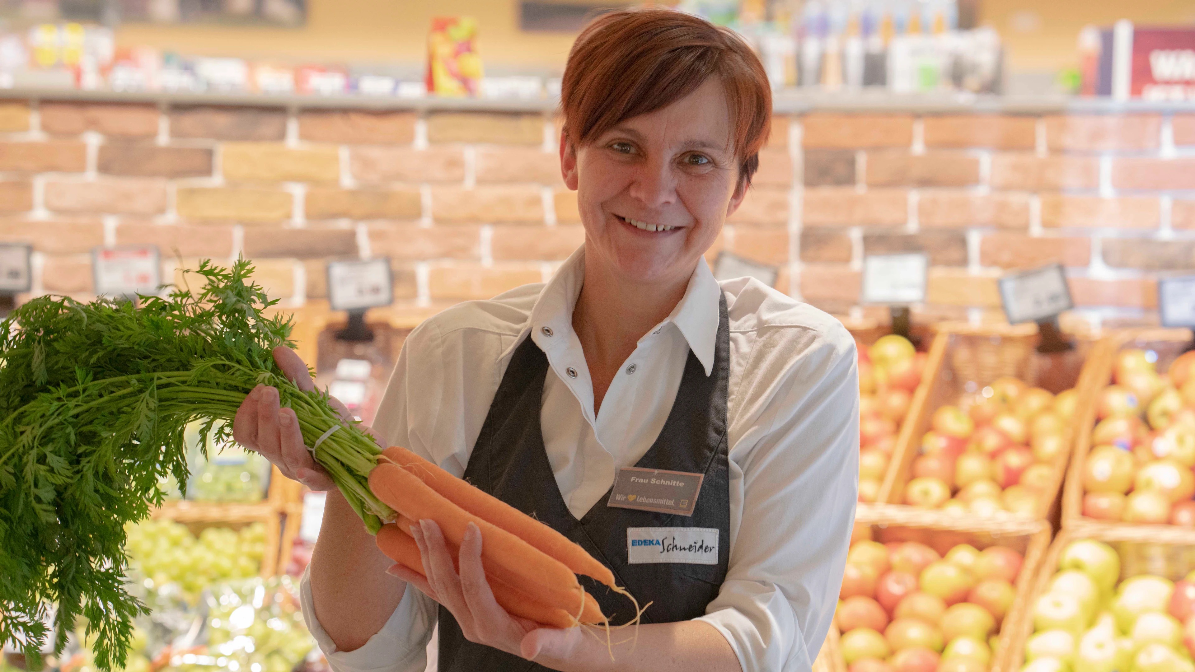 Eine lächelnde Mitarbeiterin hält ein Bund Möhren in den Händen.