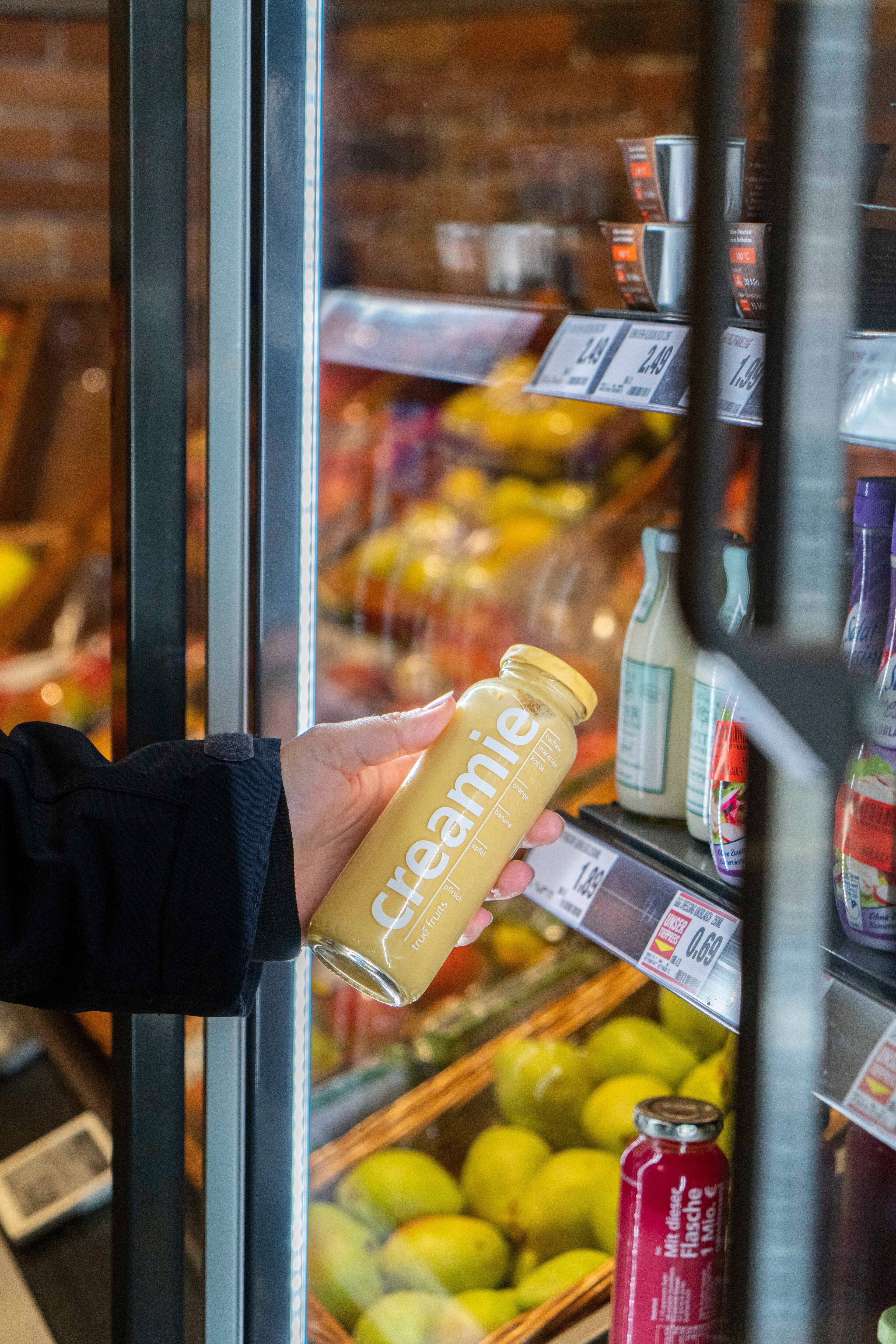 Eine Hand nimmt eines Smoothie aus einem Kühlregal.