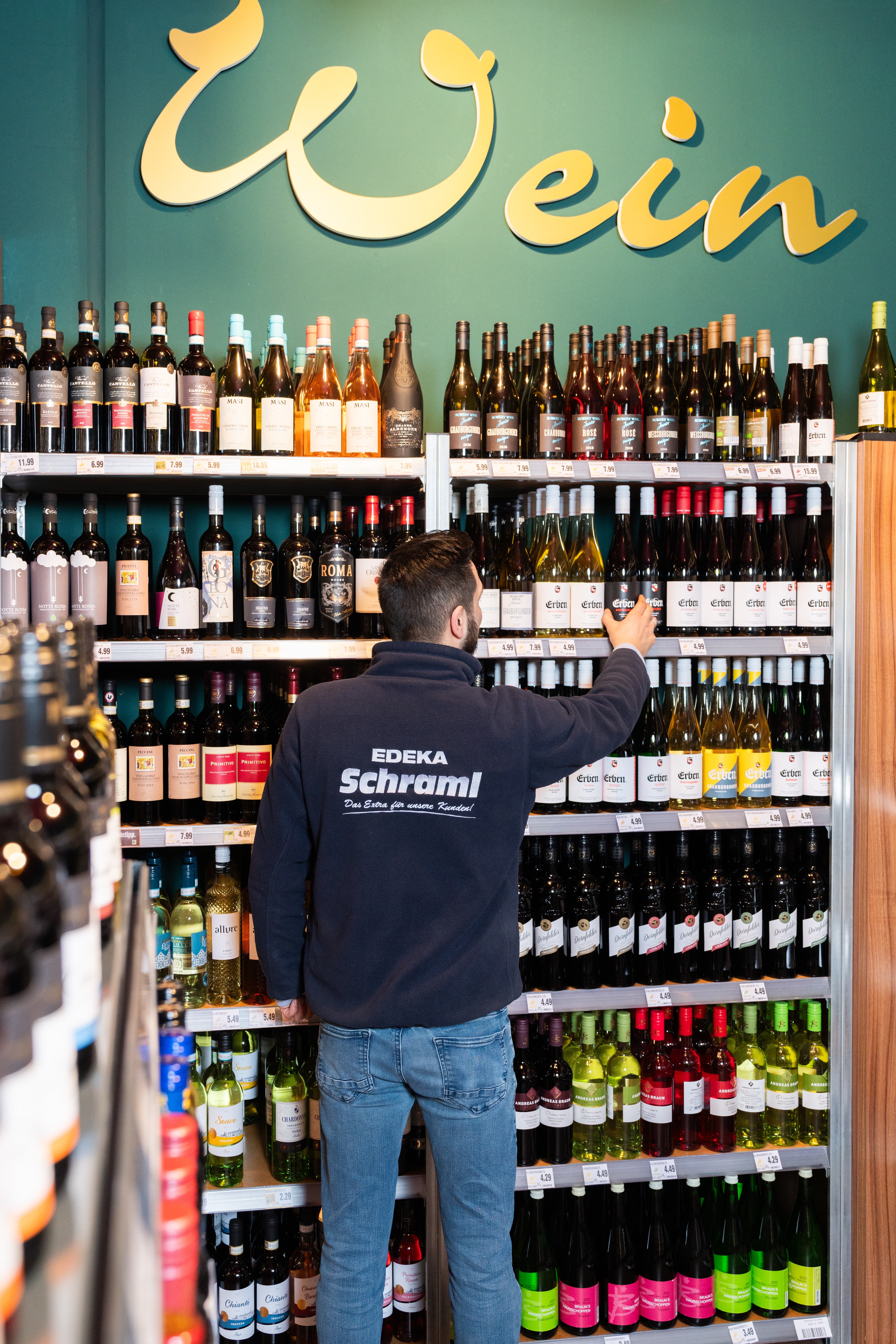 Ein Mitarbeiter eines EDEKA-Marktes stellt eine Flasche Wein in ein Regal.