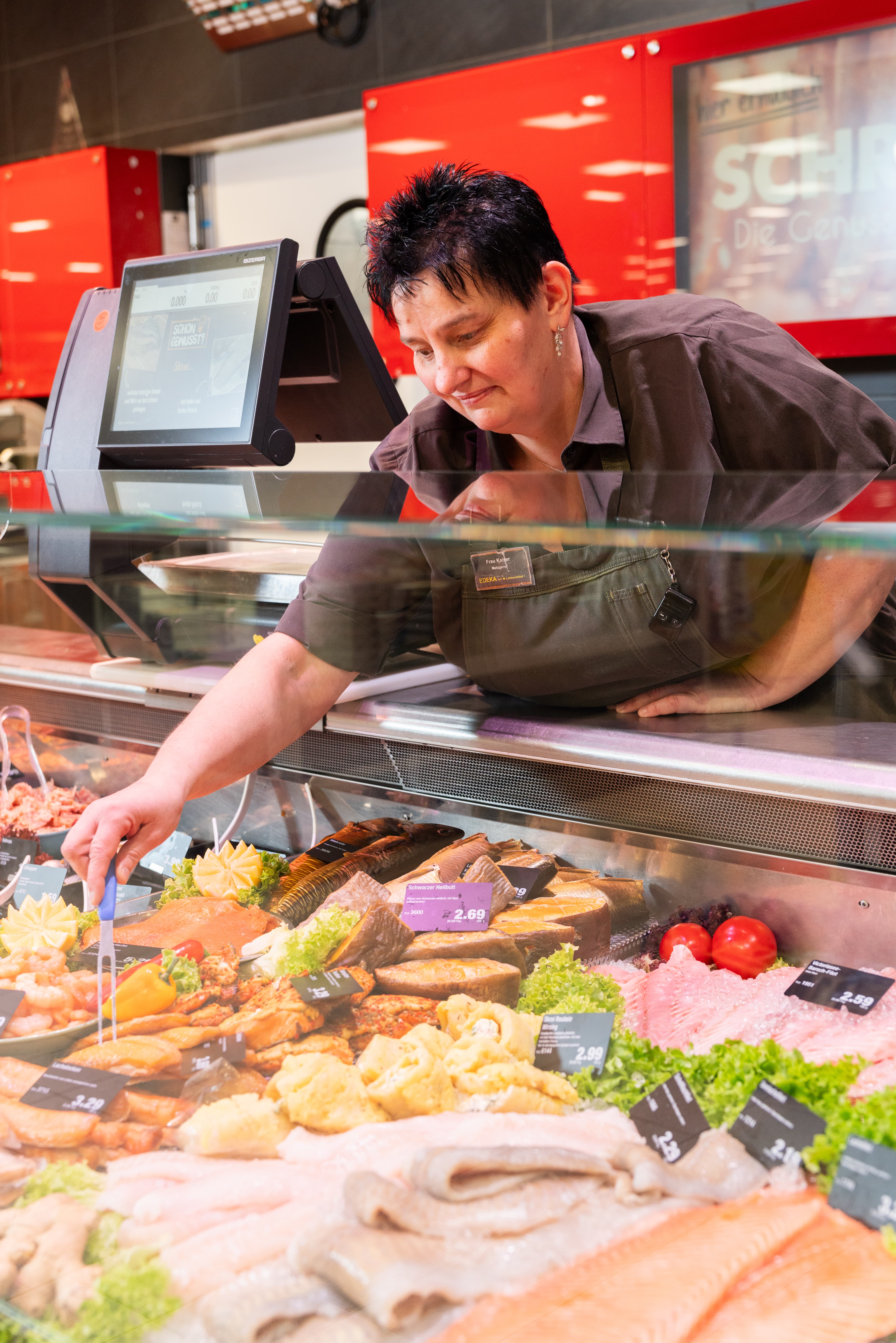 Eine Mitarbeiterin nimmt ein Stück Fisch aus der Frischetheke.