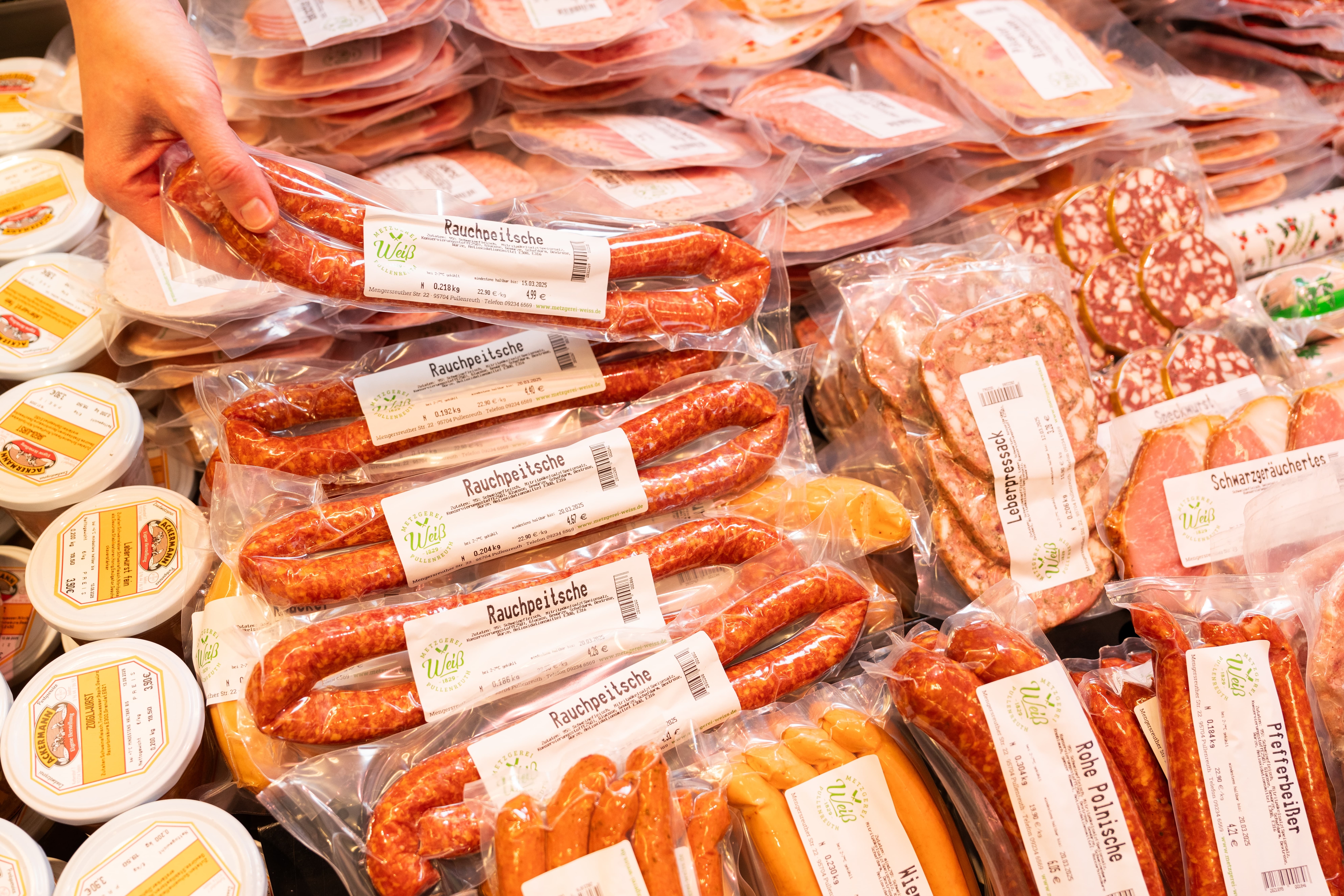 Eine Hand legt eine Wurst in die Auslage einer Wursttheke.