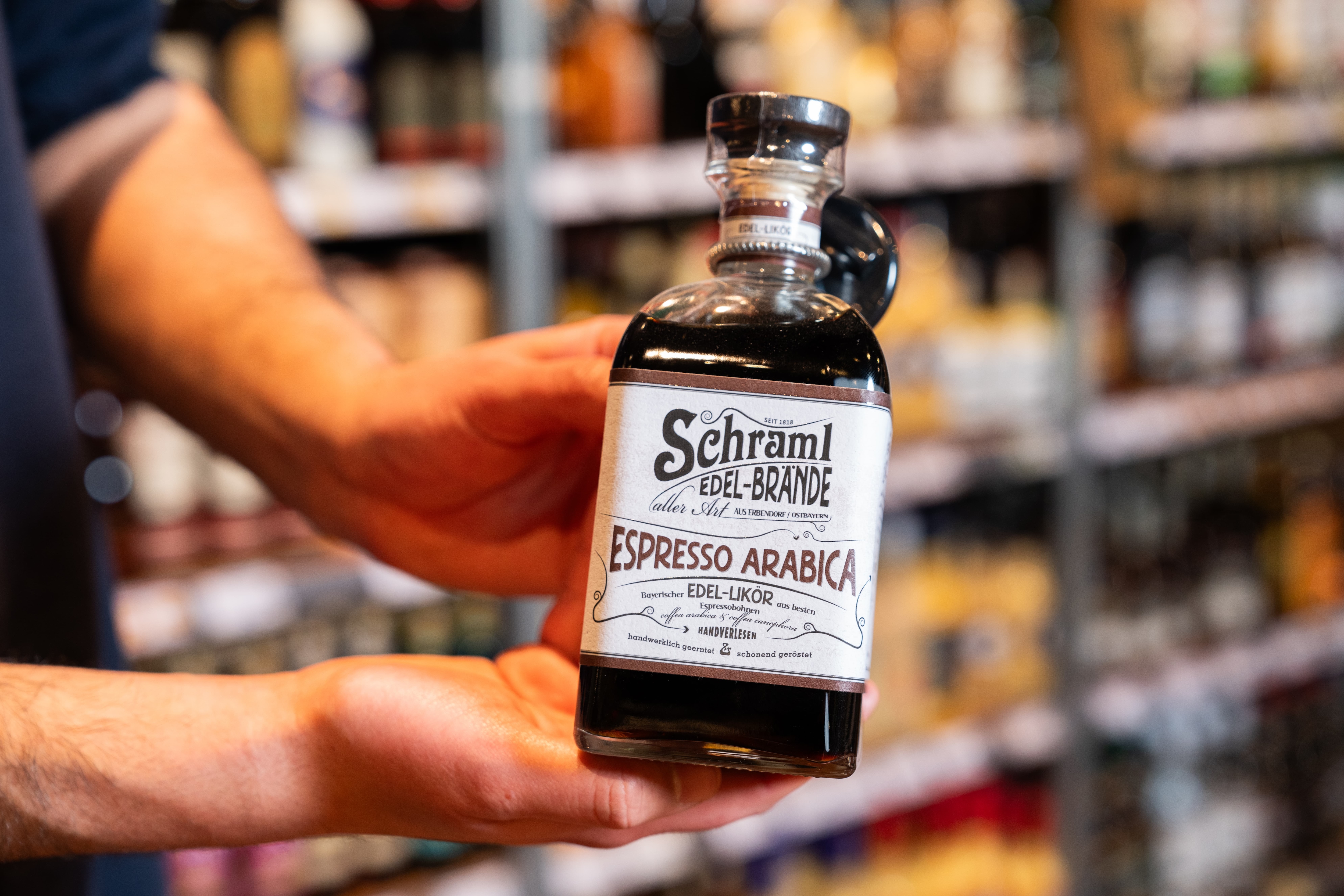 Ein Mitarbeiter hält eine Flasche Espresso Arabica von Schramls Edle Brände in der Hand.