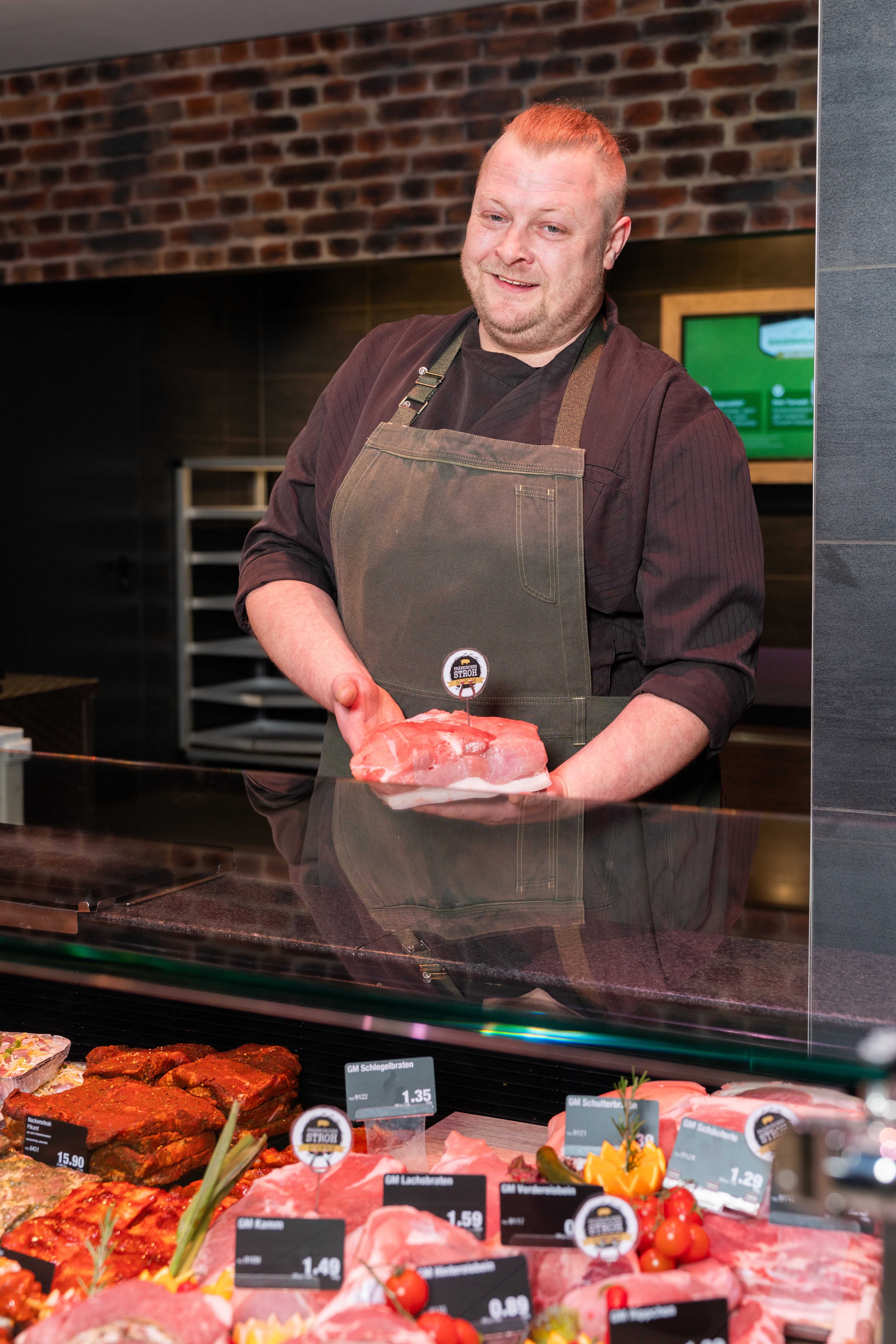 Ein lächelnder Mitarbeiter präsentiert ein Stück Fleisch hinter einer Theke.