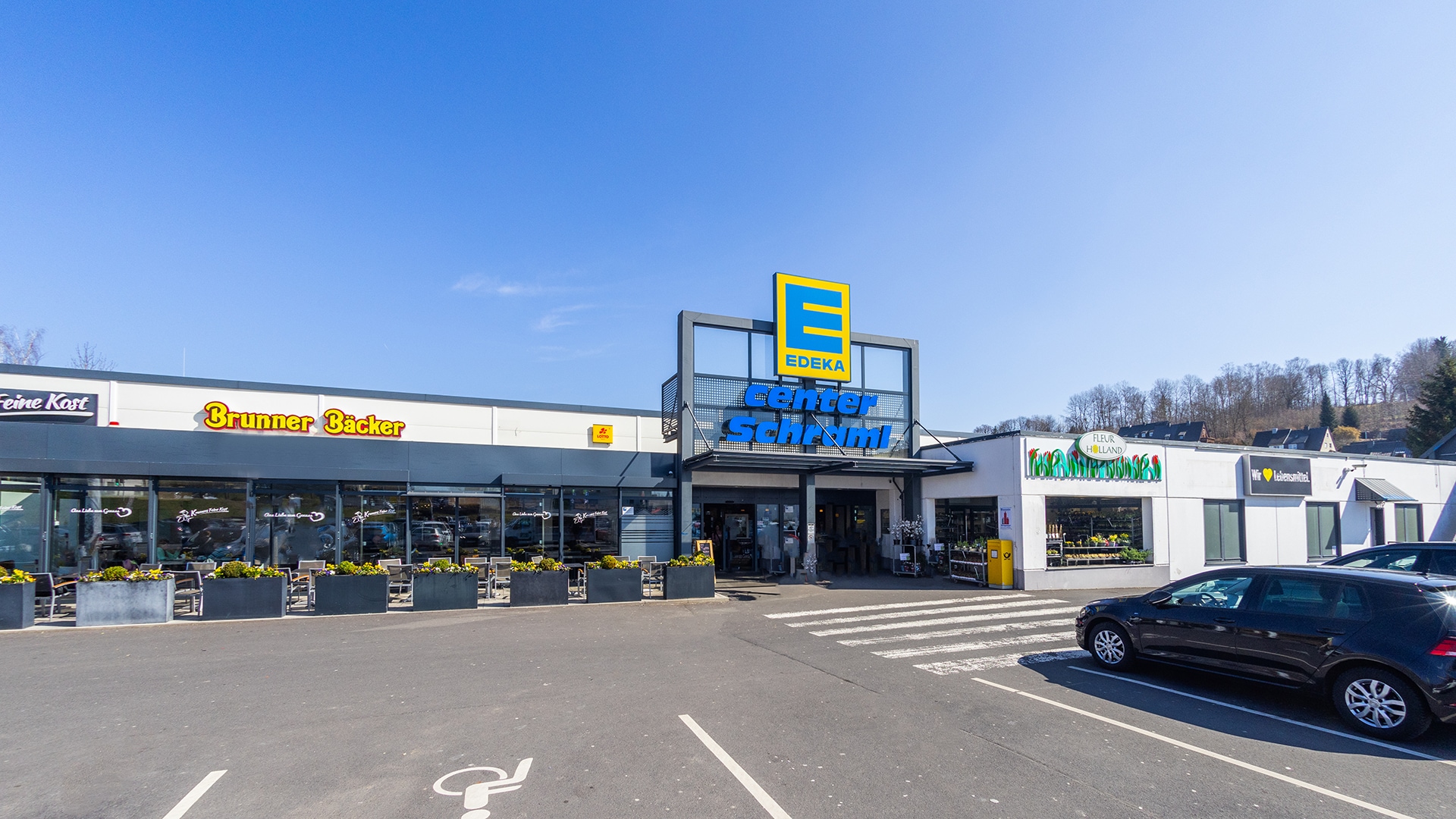 Außenansicht des Marktes mit Edeka center Schraml Schild und Parkplatz.