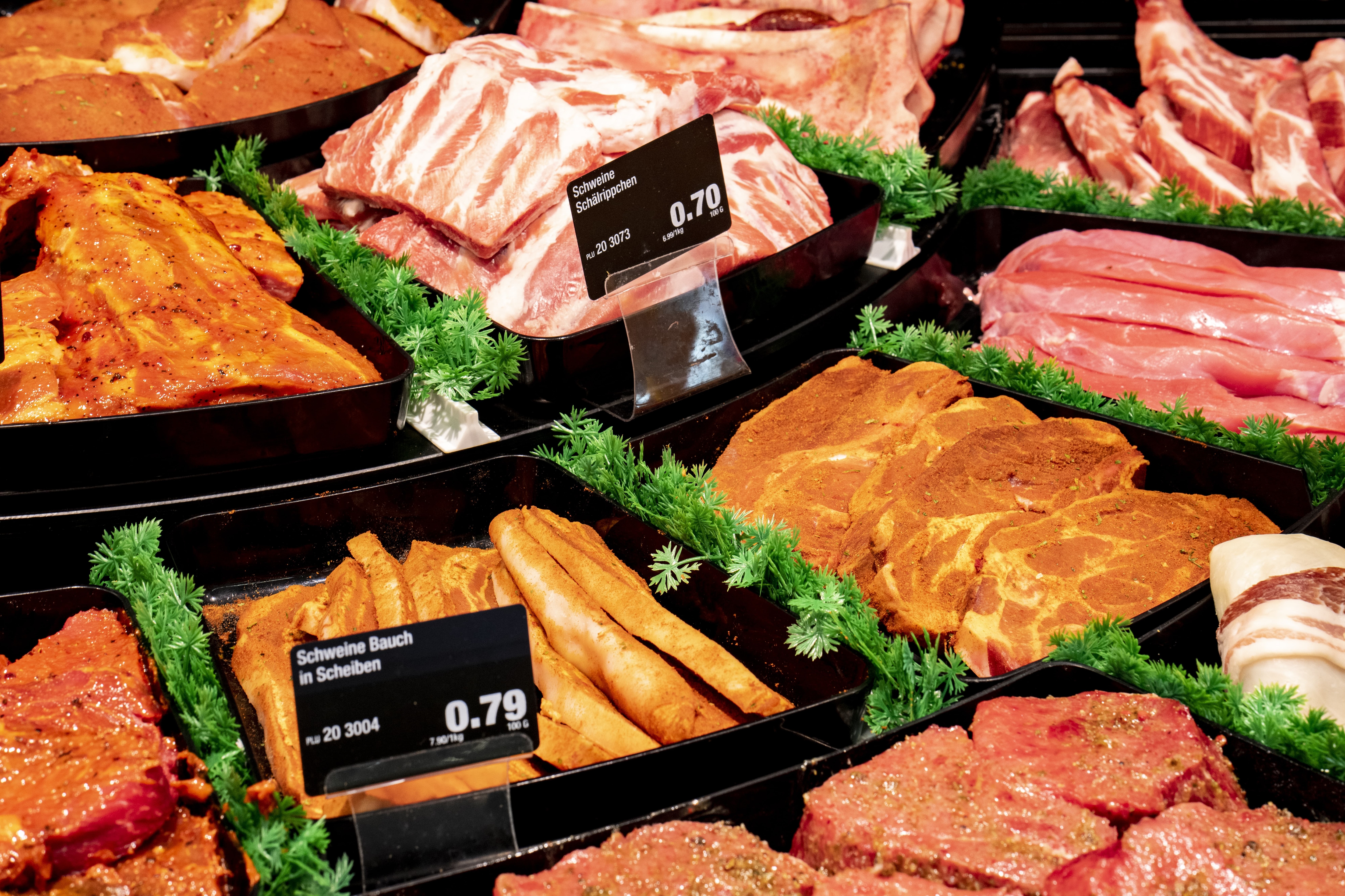 Die Fleischauslage eines EDEKA-Markts, mit Salat als Deko und Preisschildern.