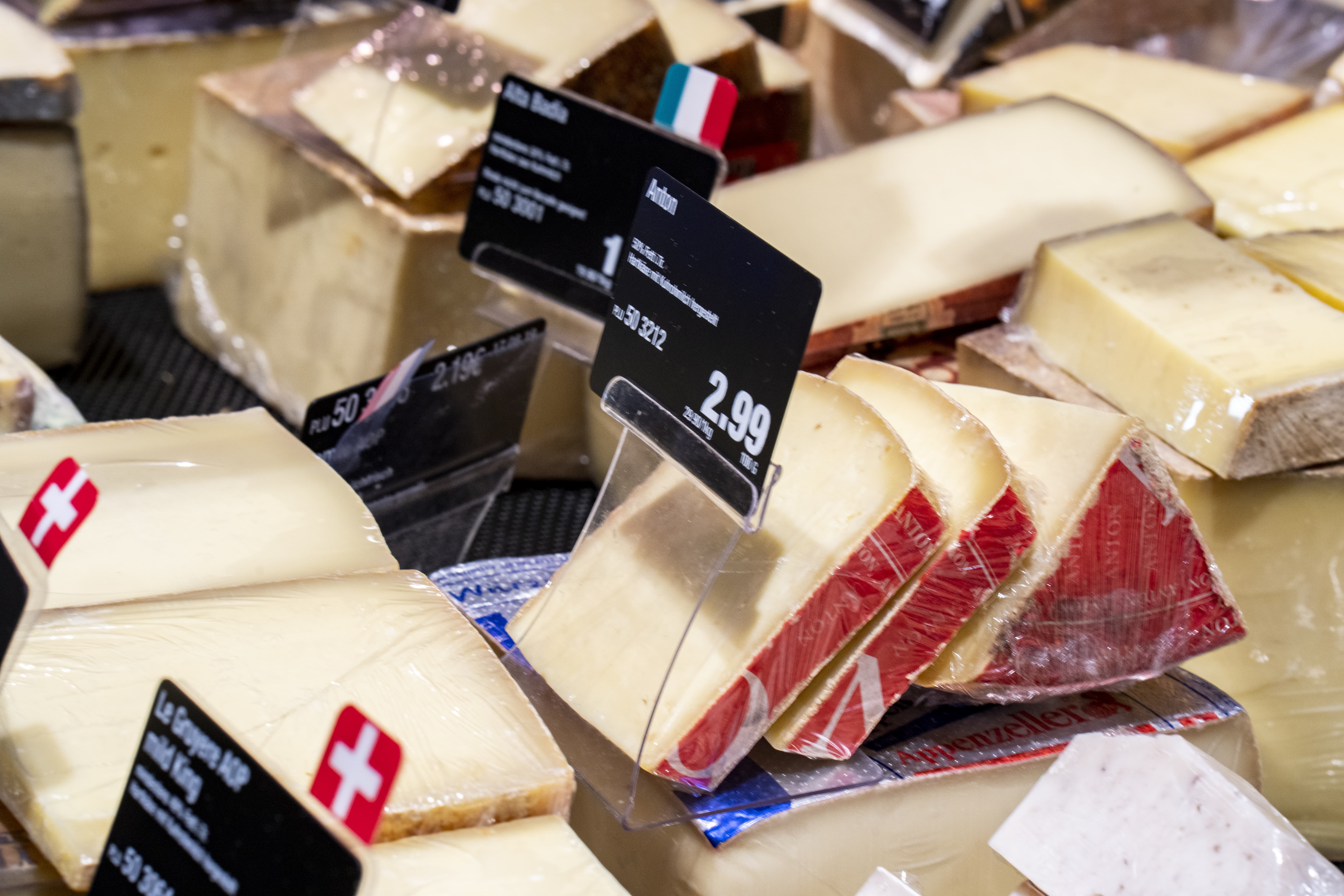 Käseauslage einer Bedienungstheke mit vielen verschiedenen Käsesorten und Preisschildern.