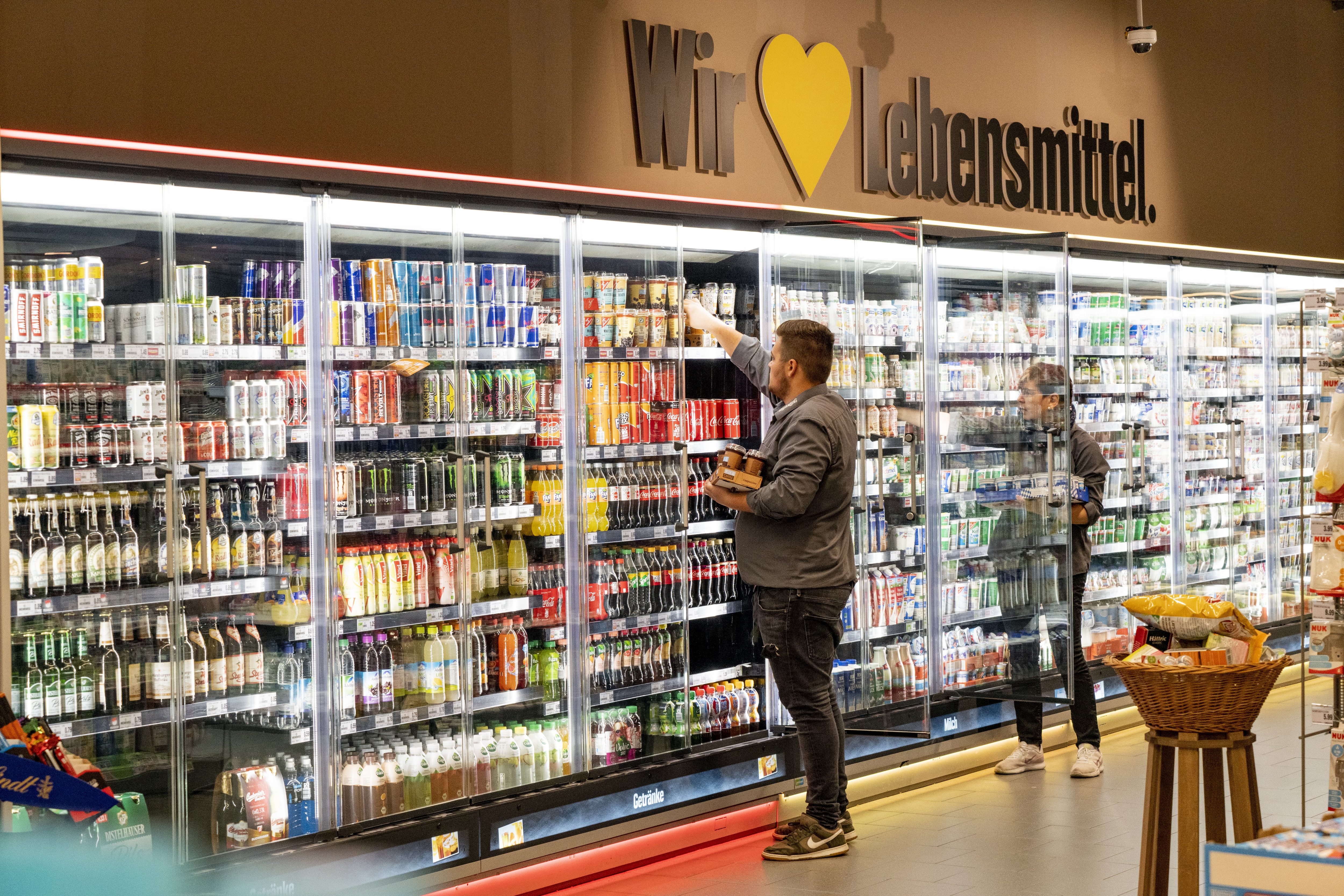 Kühlschränke mit Molkereiprodukten und Getränken in einem EDEKA-Markt. Ein Kunde und eine Kundin bedienen sich.