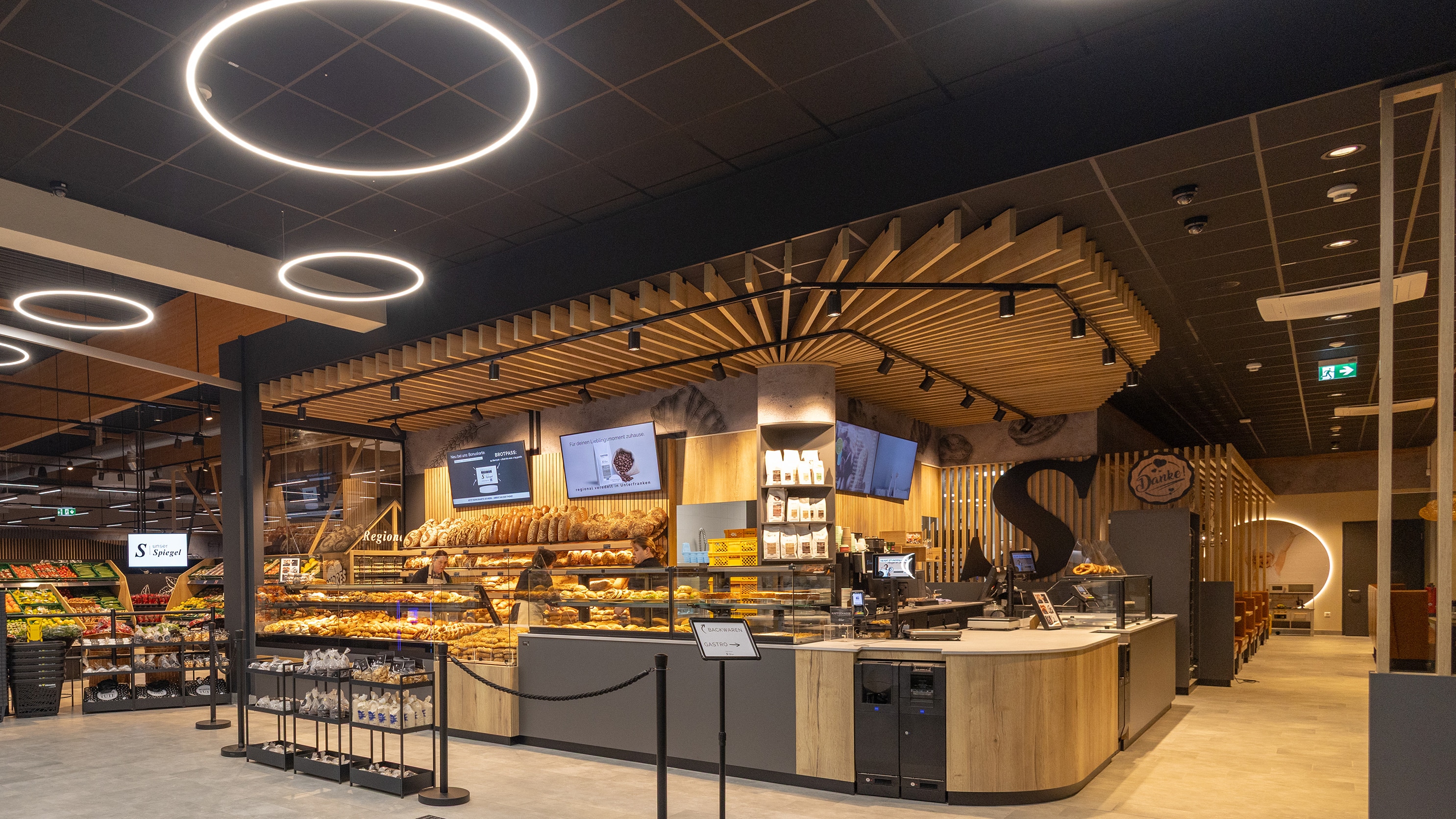 Eine großzügige Bäckertheke mit vielen frischen Broten und Backwaren, beleuchtet von runden Deckenleuchten.