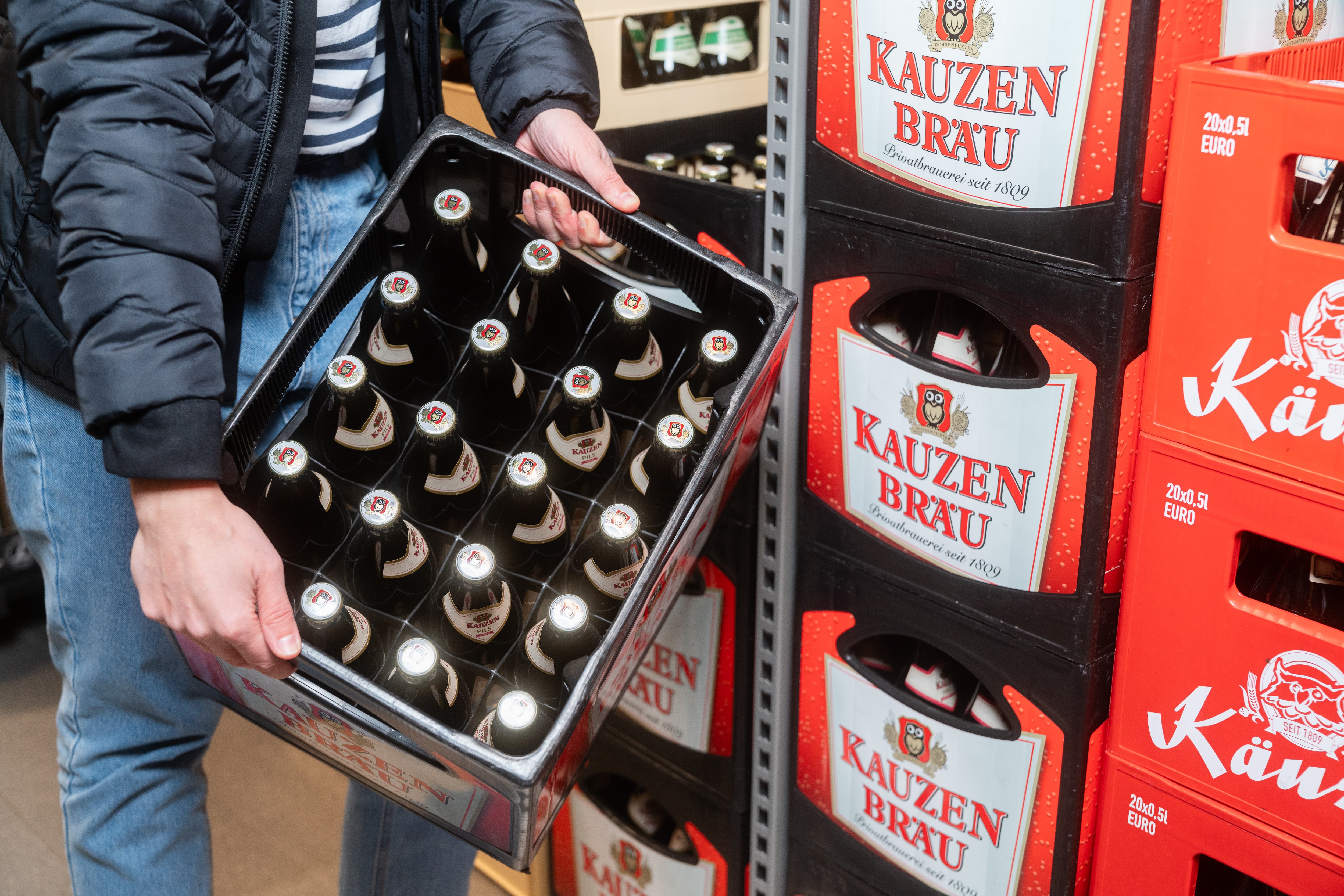 Zwei Hände halten eine Kiste mit 20 Bierflaschen der Marke Kauzen Bräu.