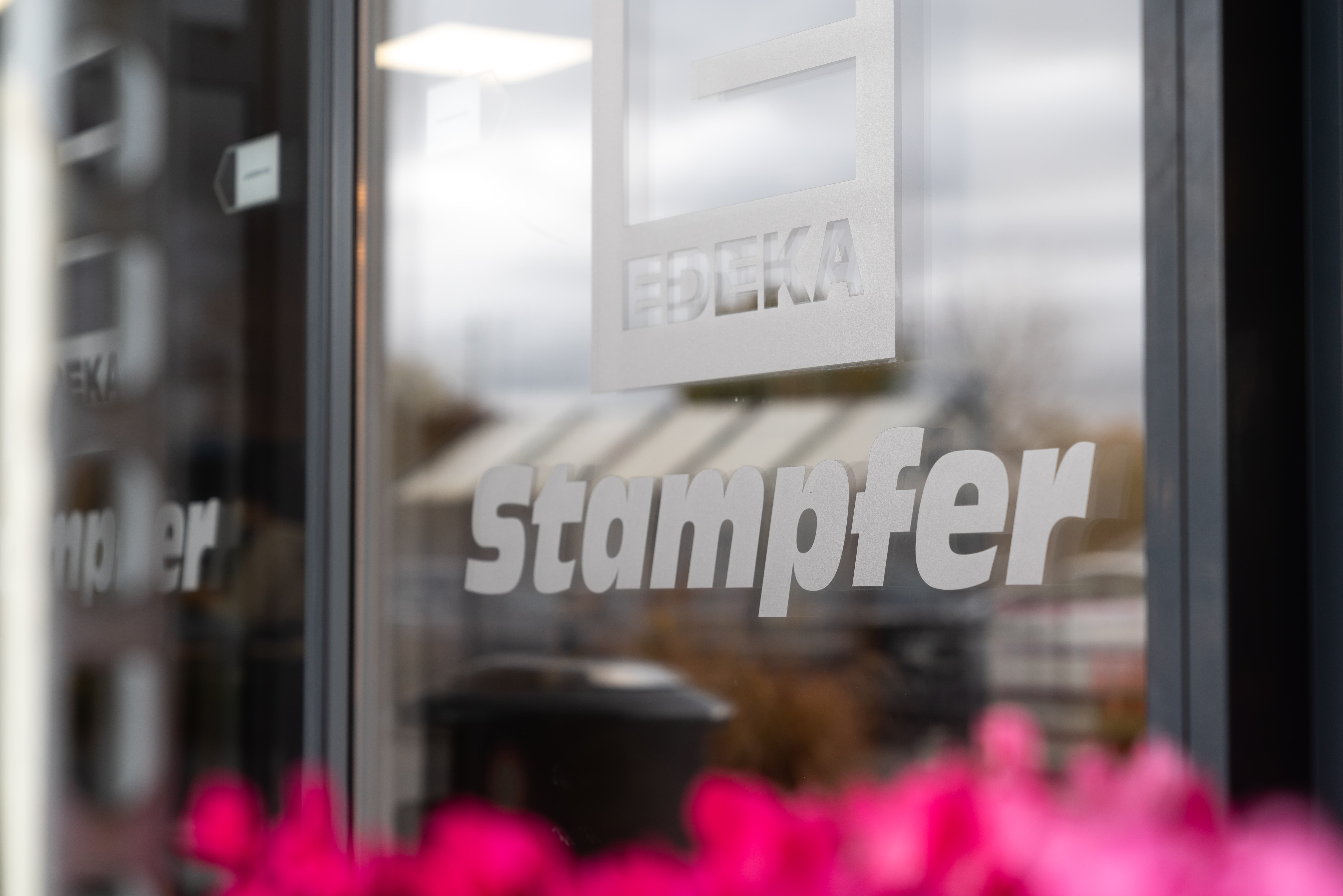 Blick von außen auf eine Scheibe der automatischen Eingangstür mit EDEKA-Logo und dem Schriftzug Stampfer.