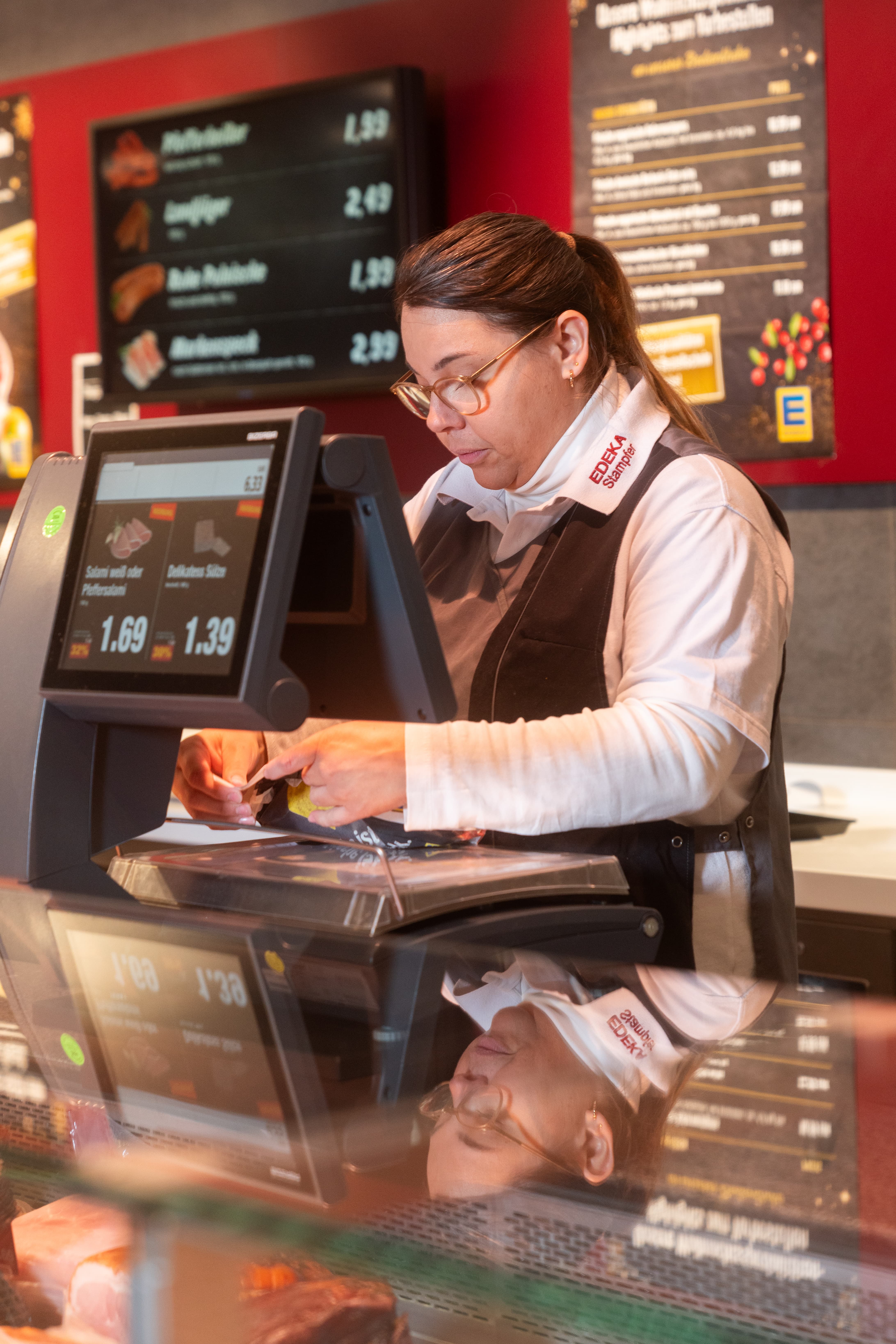 Eine Frau in EDEKA-Kleidung steht an der Waage hinter der Frischetheke.