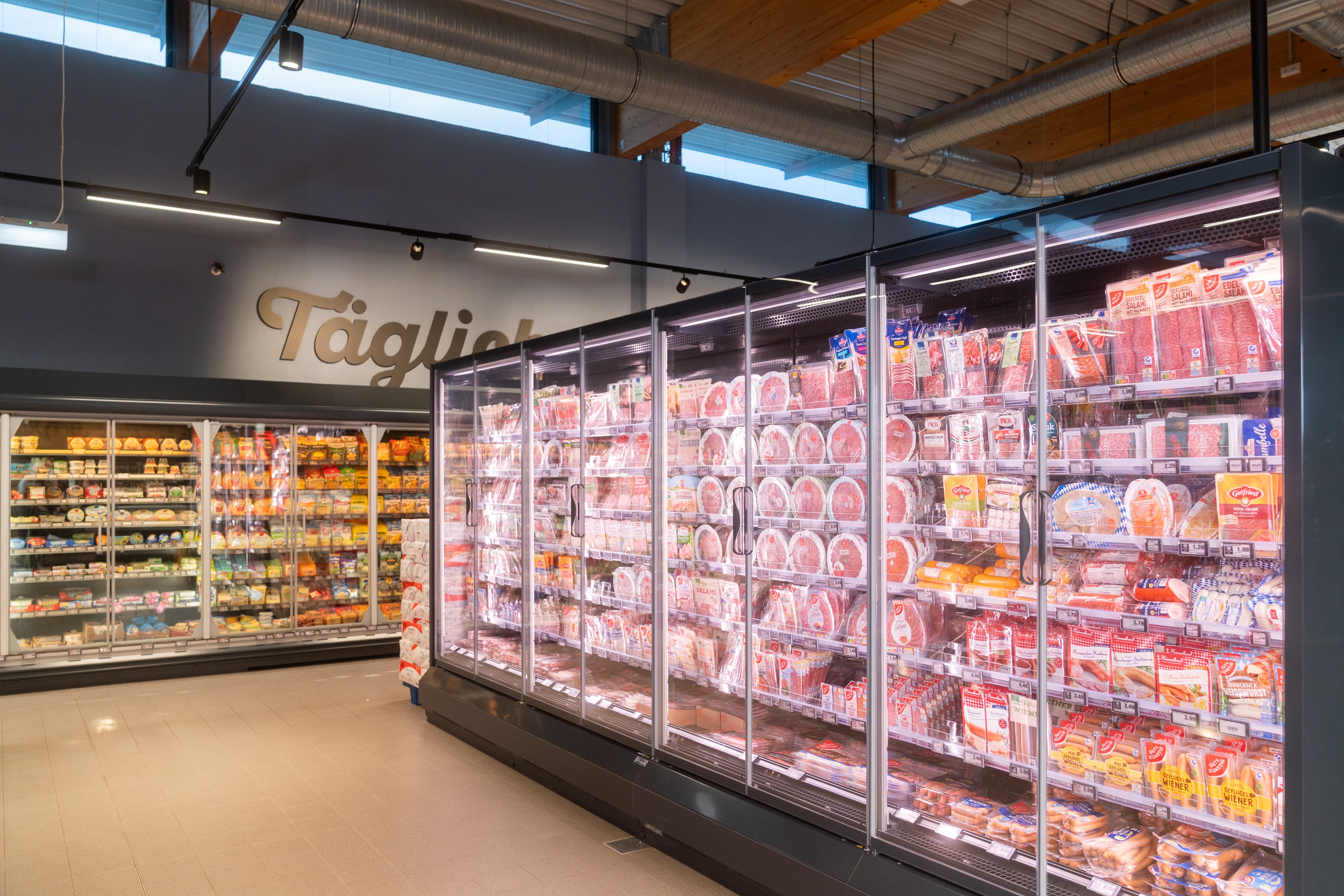 Kühlschränke mit Wurstaufschnitt in einem Quergang. An der Stirnseite Käsekühlschränke.